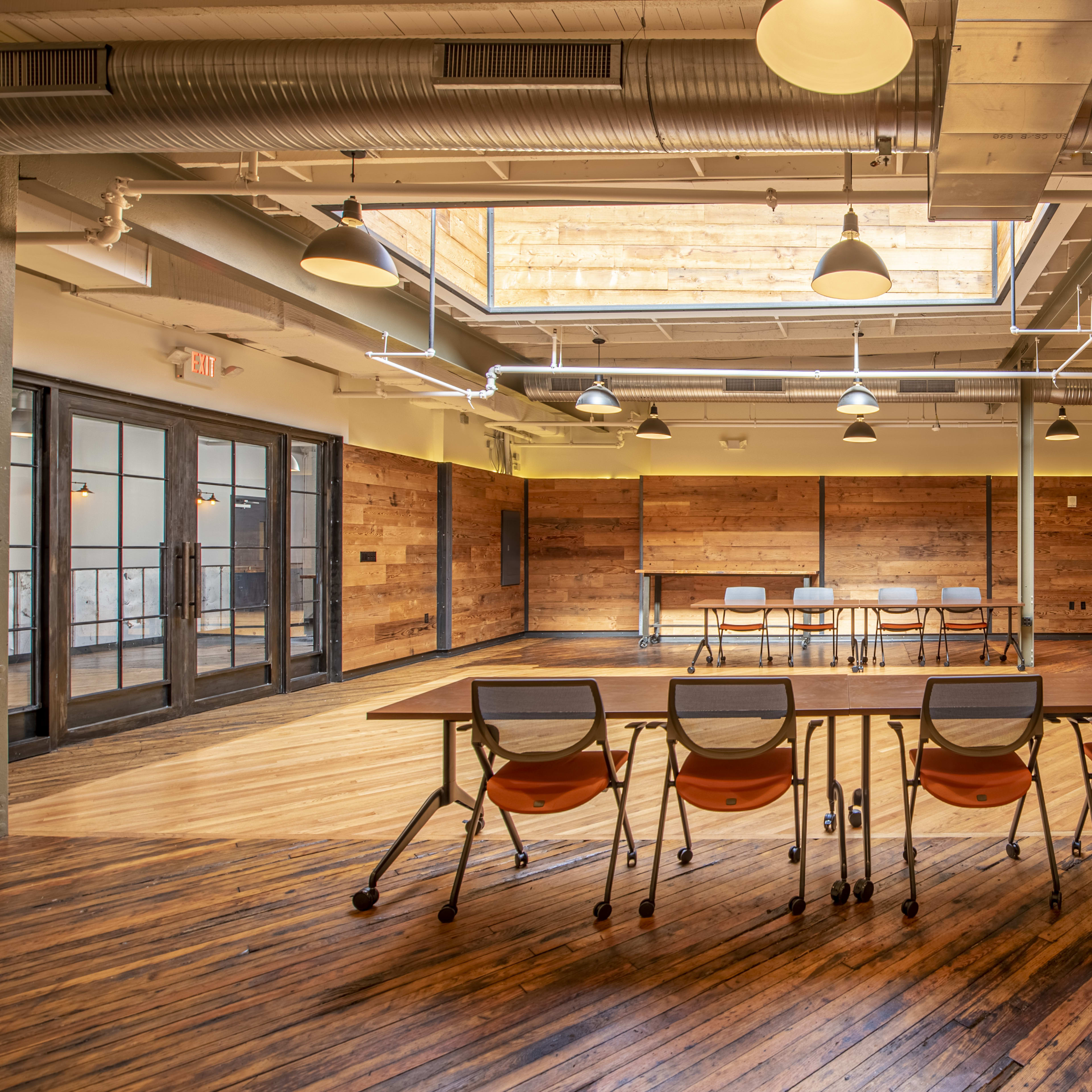 A spacious meeting room with wooden floors, a large table surrounded by chairs, and a modern fireplace along one wall.