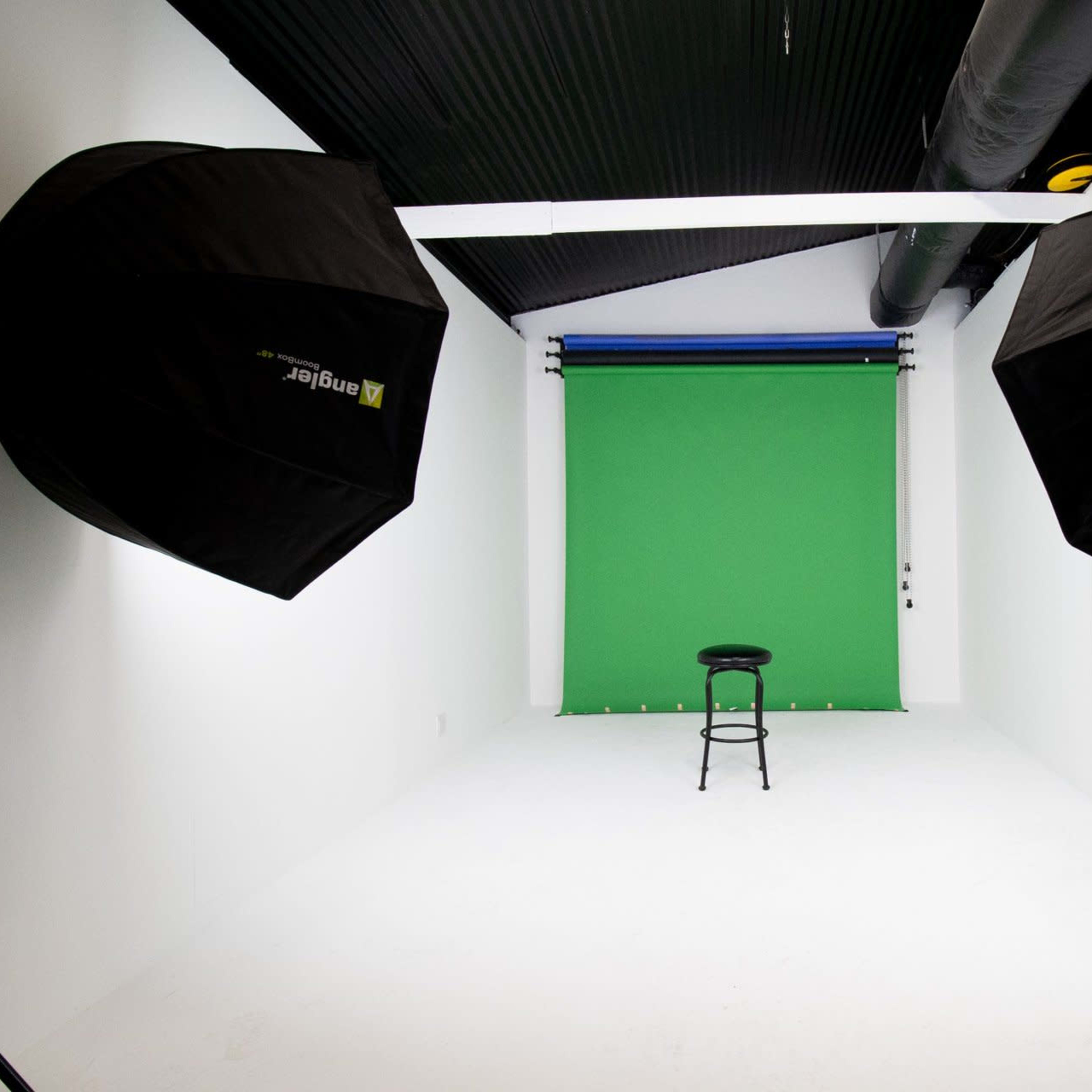 A photography studio with a green backdrop, a black stool in the center, and two large softbox lights on either side.