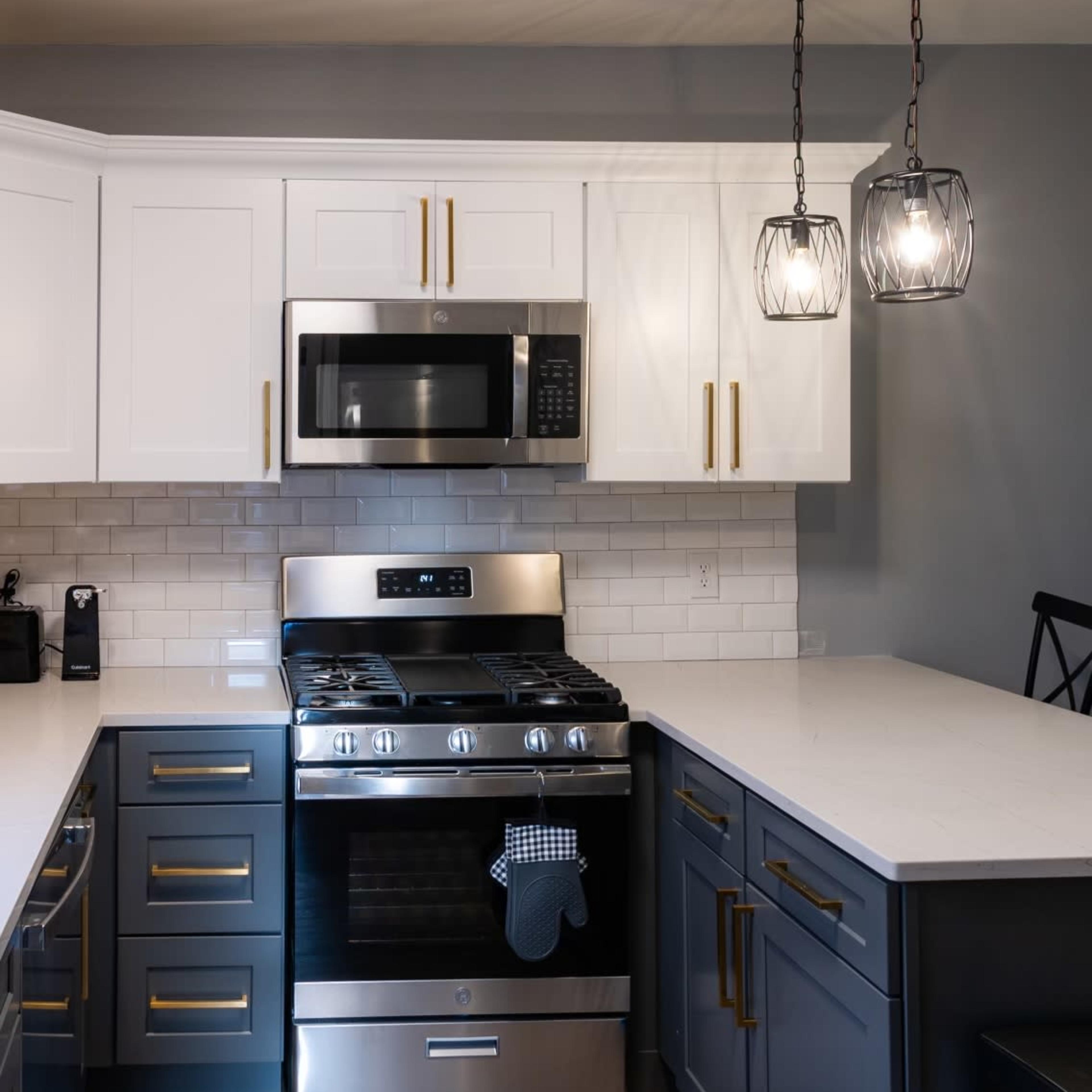 A modern kitchen with white and gray cabinetry, a stainless steel gas stove, microwave, and pendant lighting above an island.
