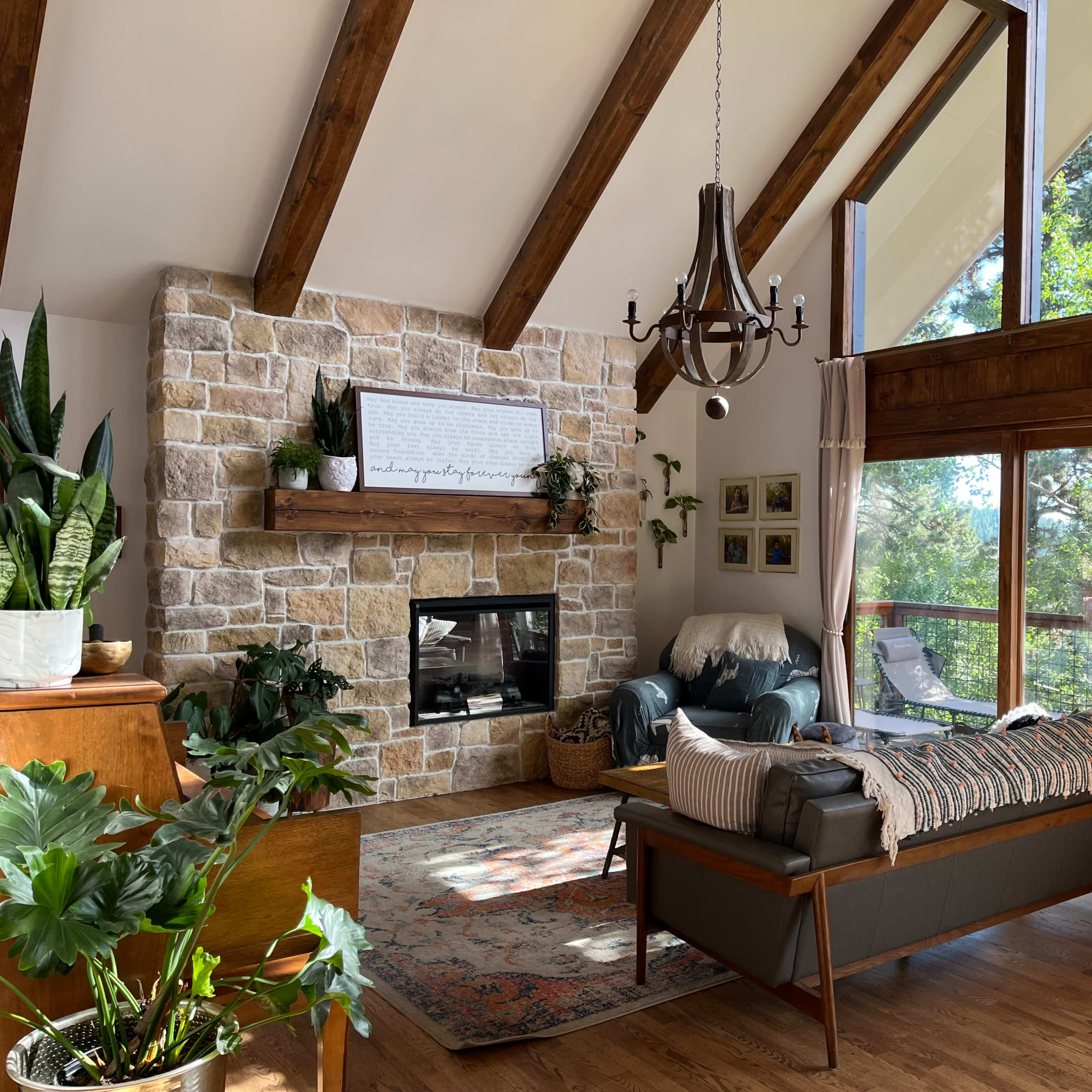 A spacious living room features a stone fireplace, large windows with views of greenery, and comfortable seating options.