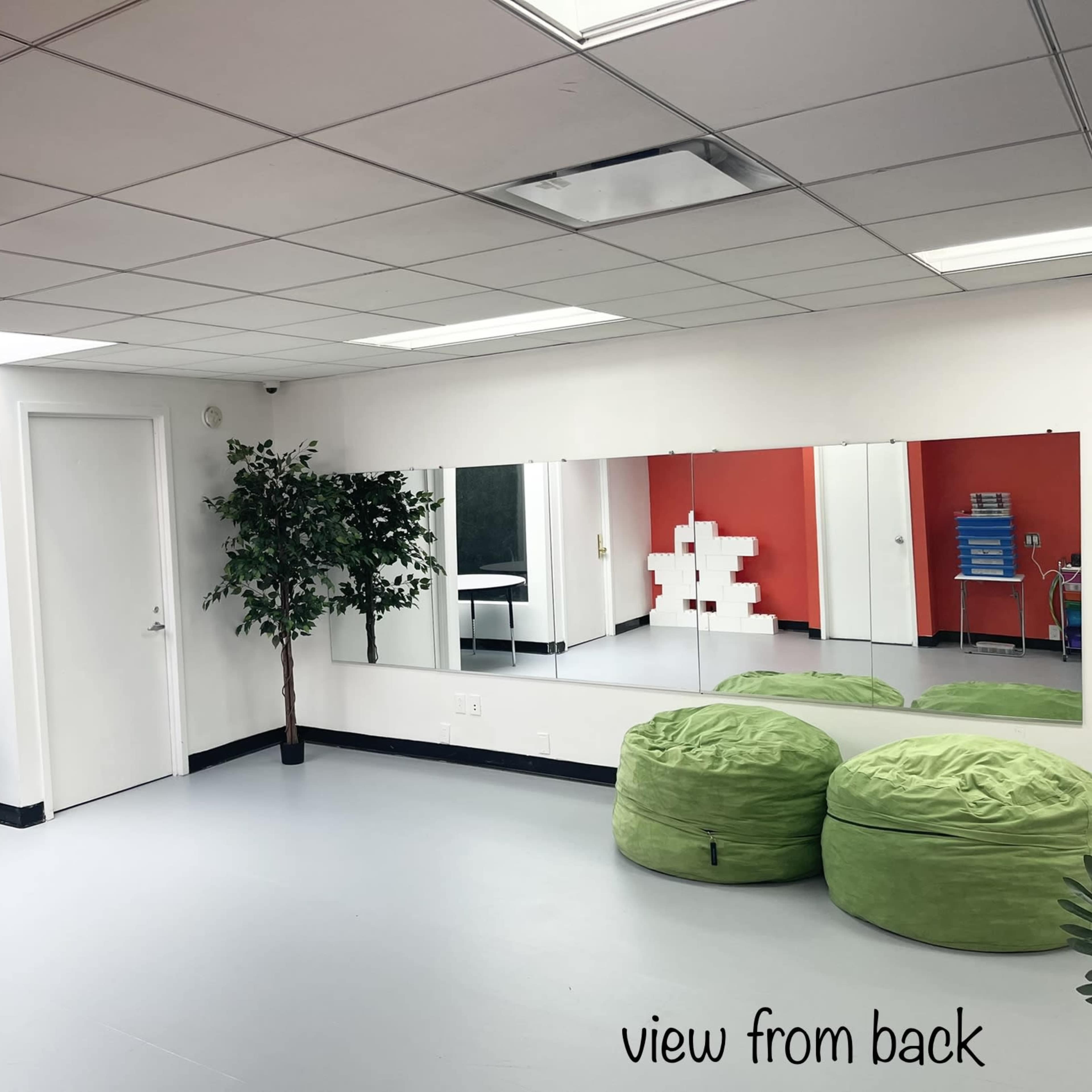 A room with green wall decor, a table, bean bags, mirrors, and an exit sign.