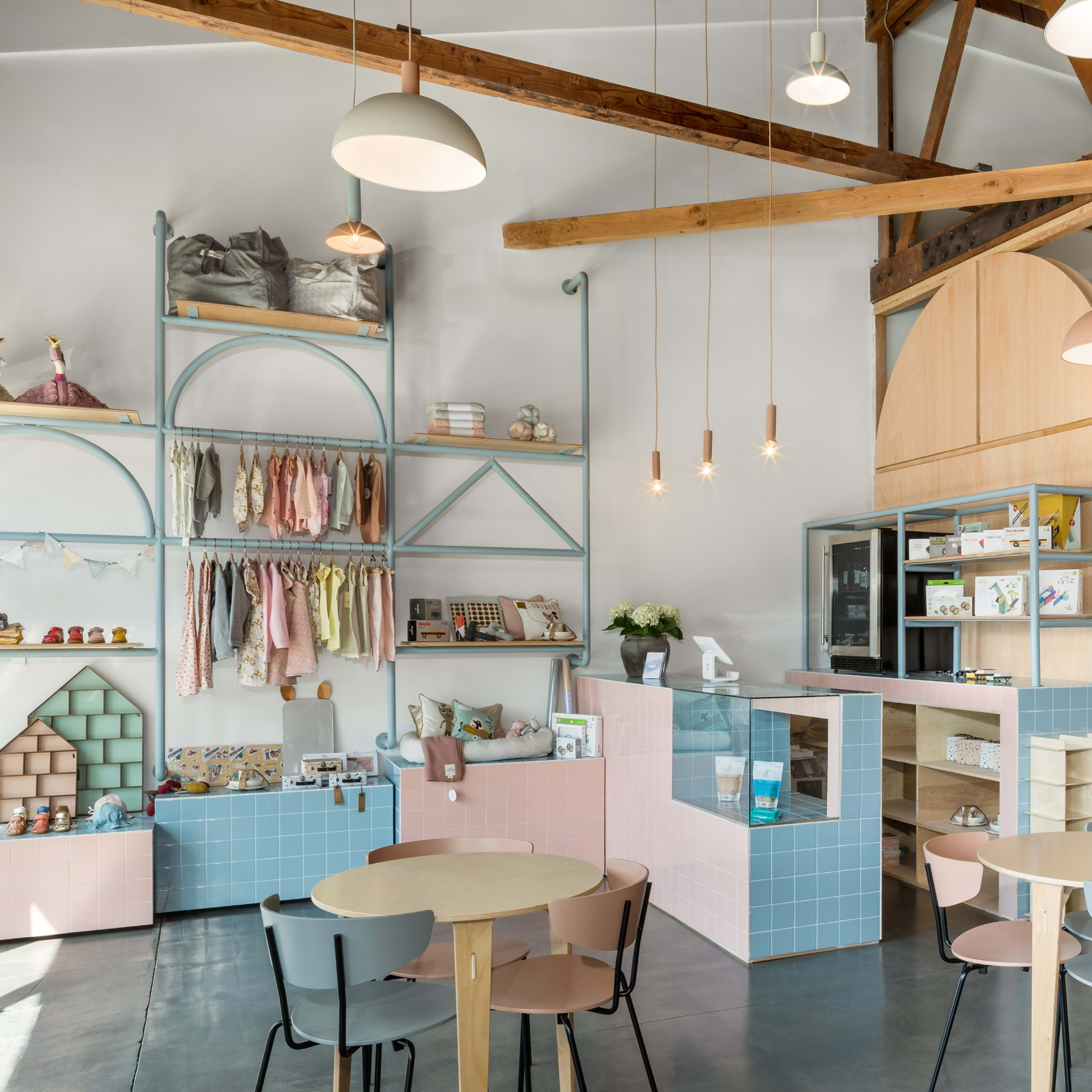 A modern children's store featuring wooden beams, colorful shelving displaying clothes and toys, and a play area with a slide and climbing structure.