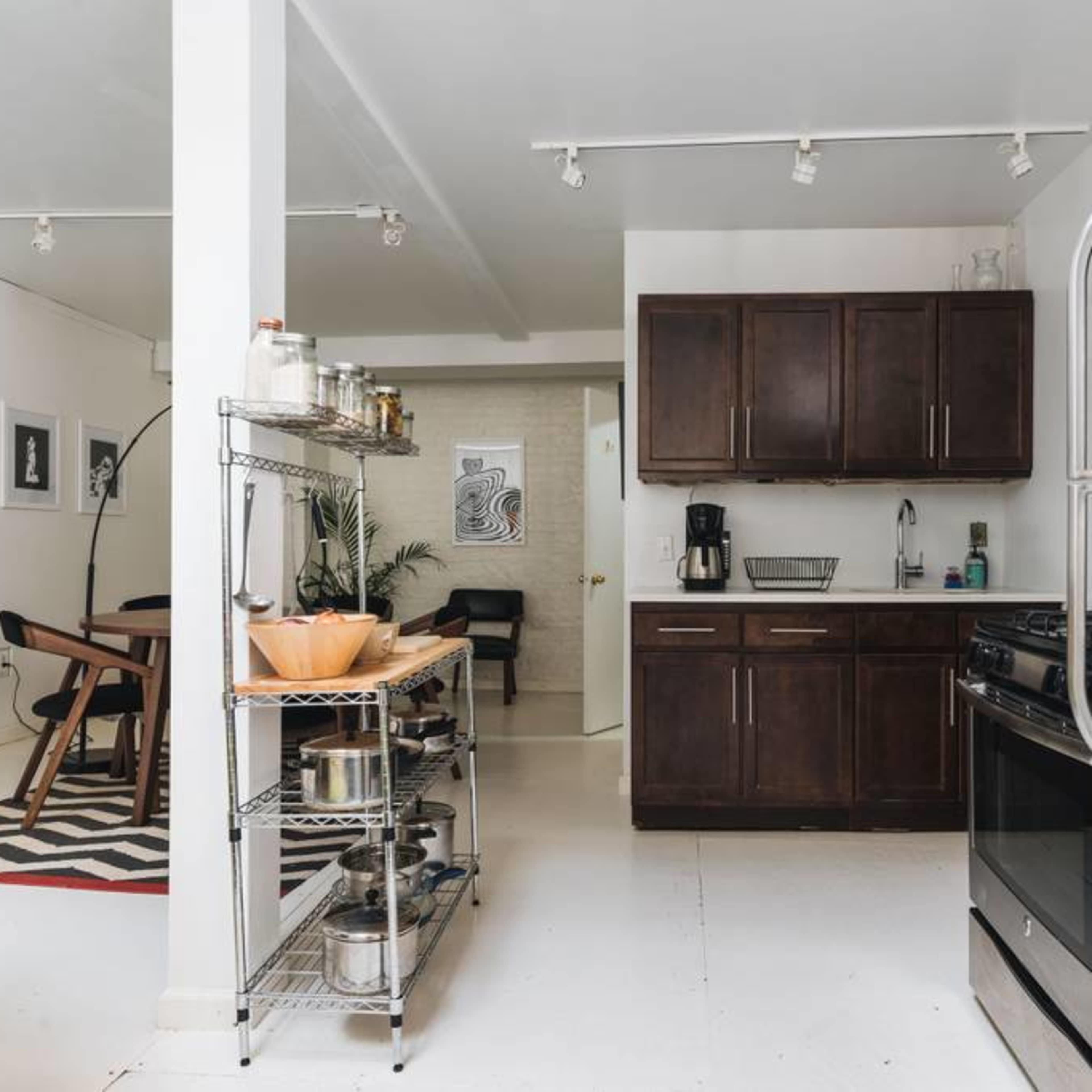 A modern kitchen with dark wood cabinets, a stainless steel refrigerator, and an open layout connecting to a dining area with a patterned rug.
