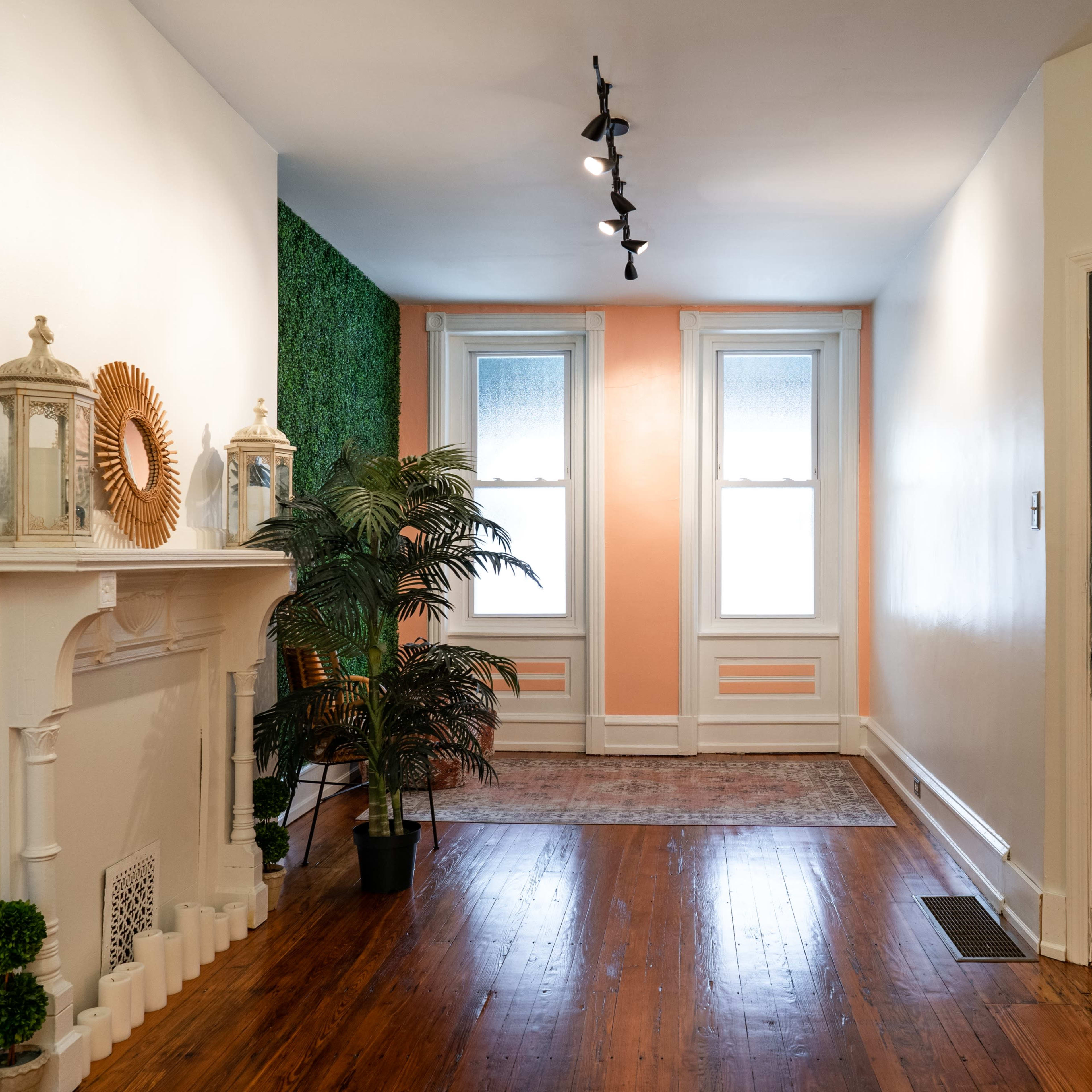 A bright hallway with a fireplace, two windows, a green accent wall, and a dark door adorned with decorative hooks.