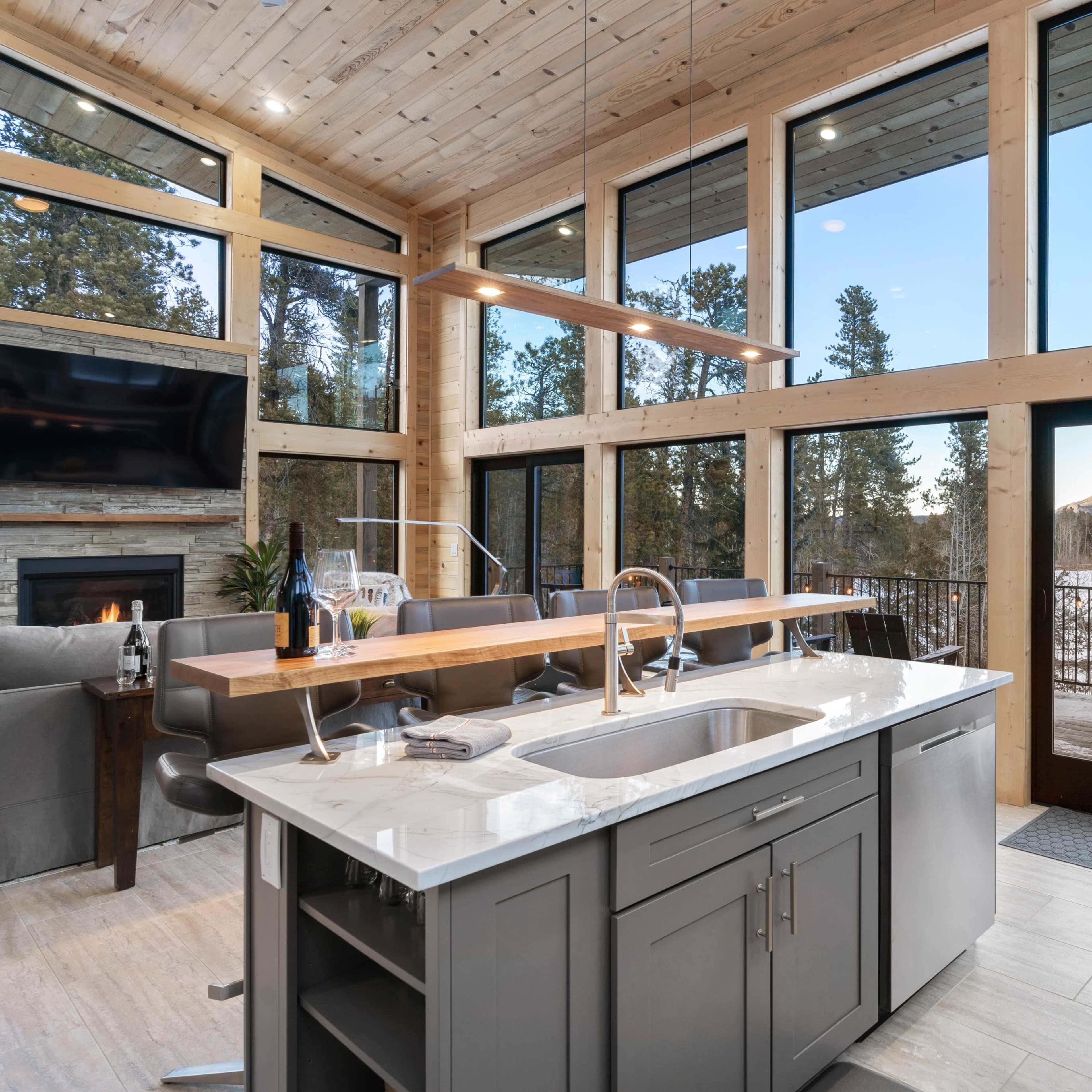 A modern kitchen with large windows overlooking a snowy landscape, featuring a central island and wooden cabinetry.