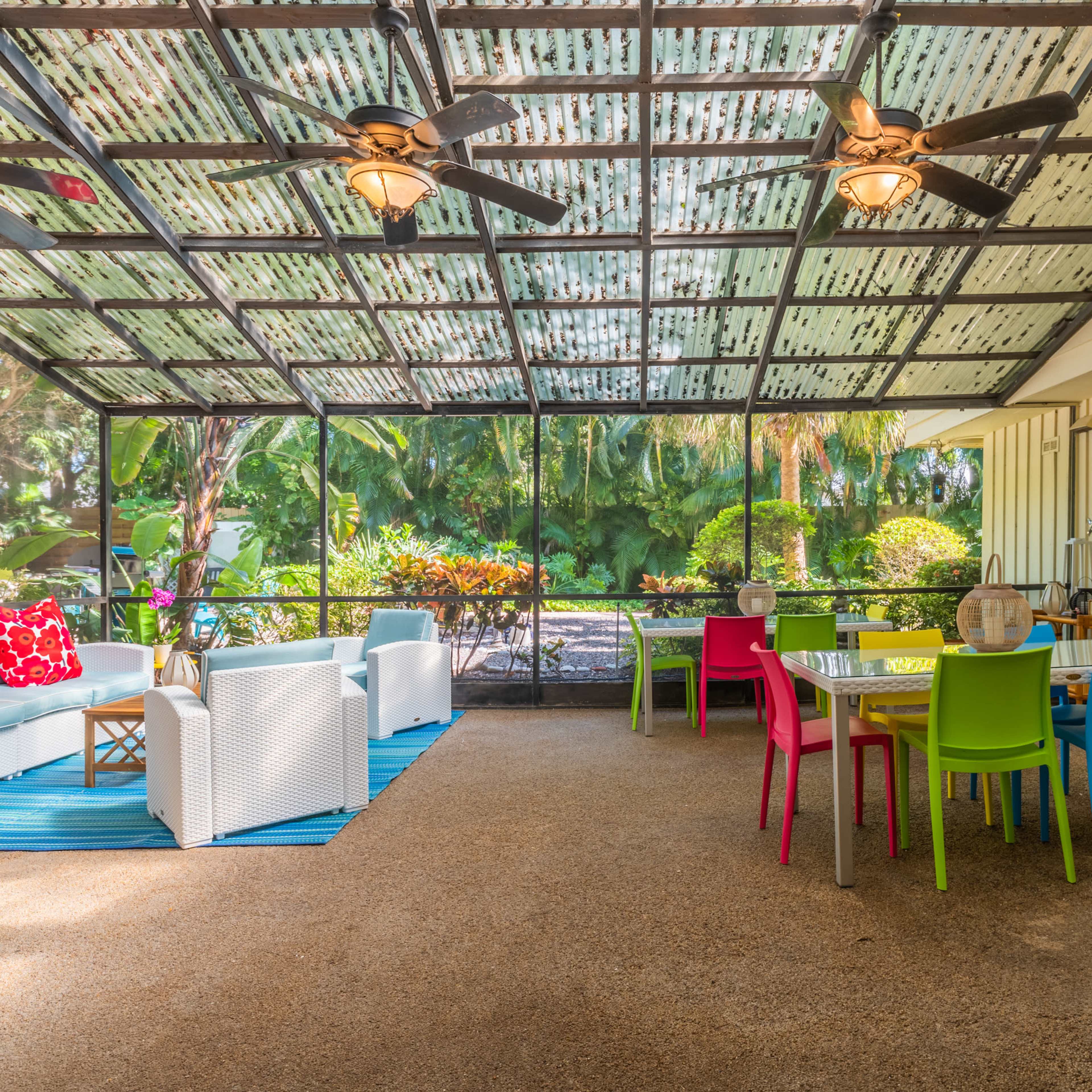 A screened porch featuring colorful chairs and a dining table set within a lush garden setting.