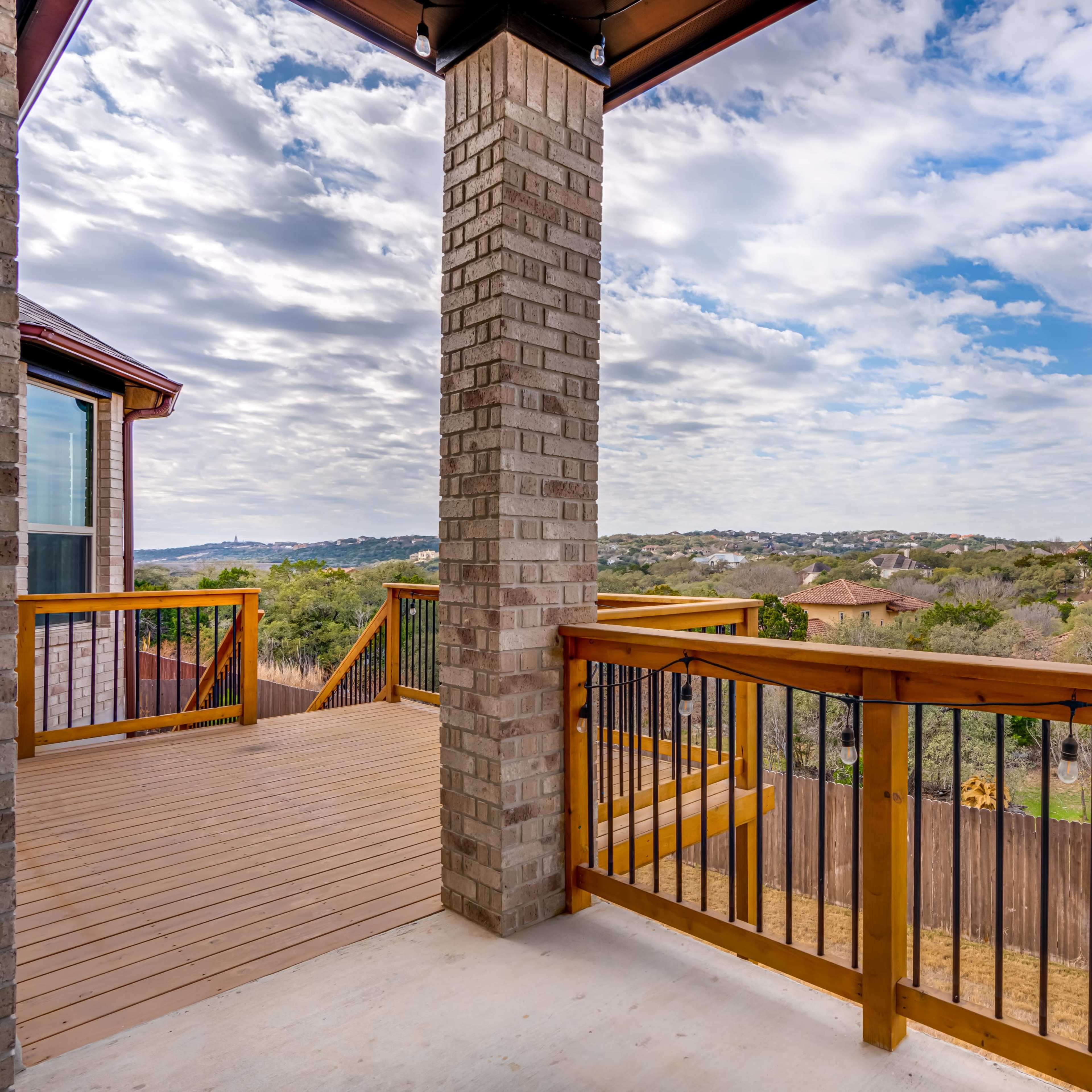 A balcony with wooden railings overlooking a hilly landscape and cloudy sky.