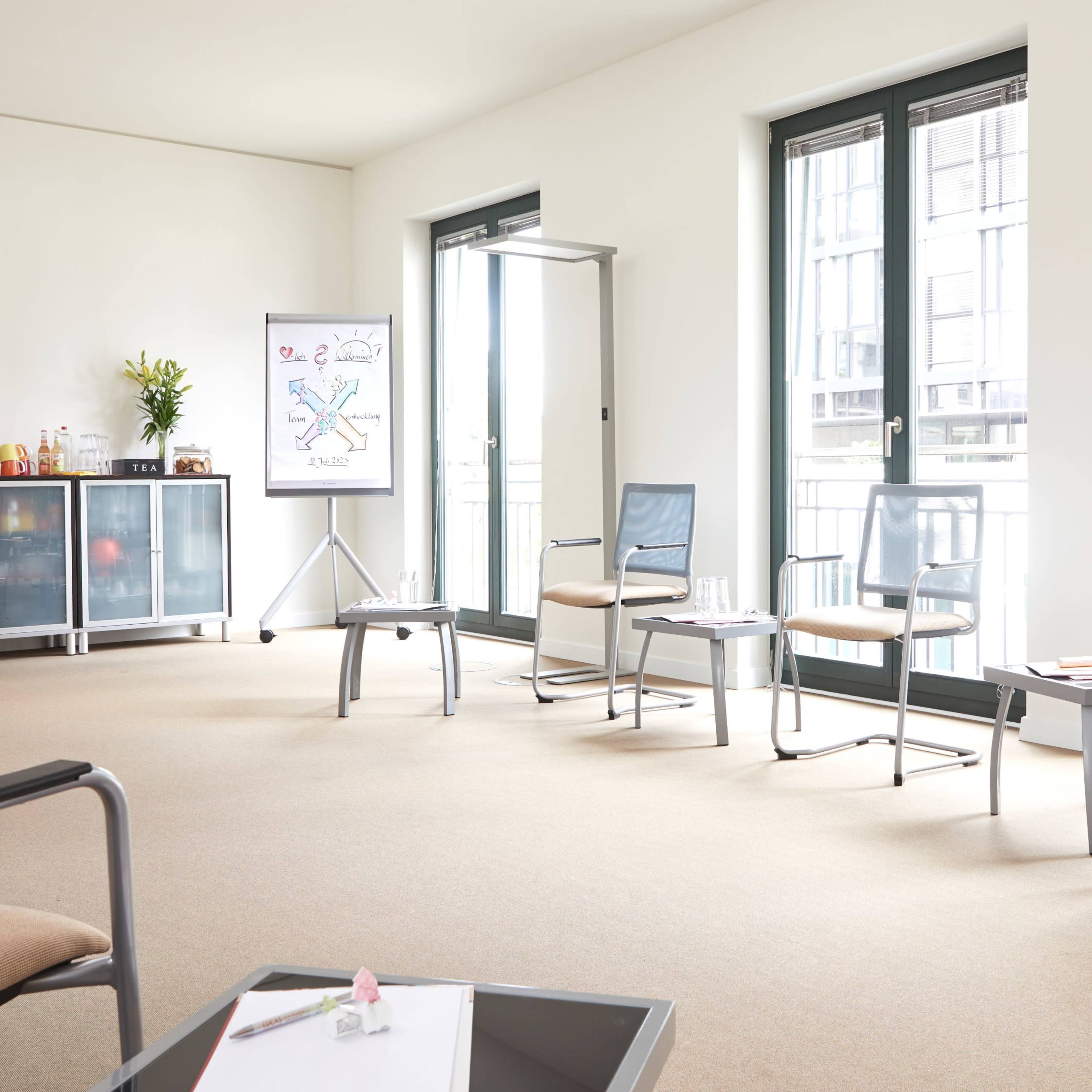 A bright, spacious waiting room with several chairs arranged around a coffee table, a presentation board, and storage cabinets.