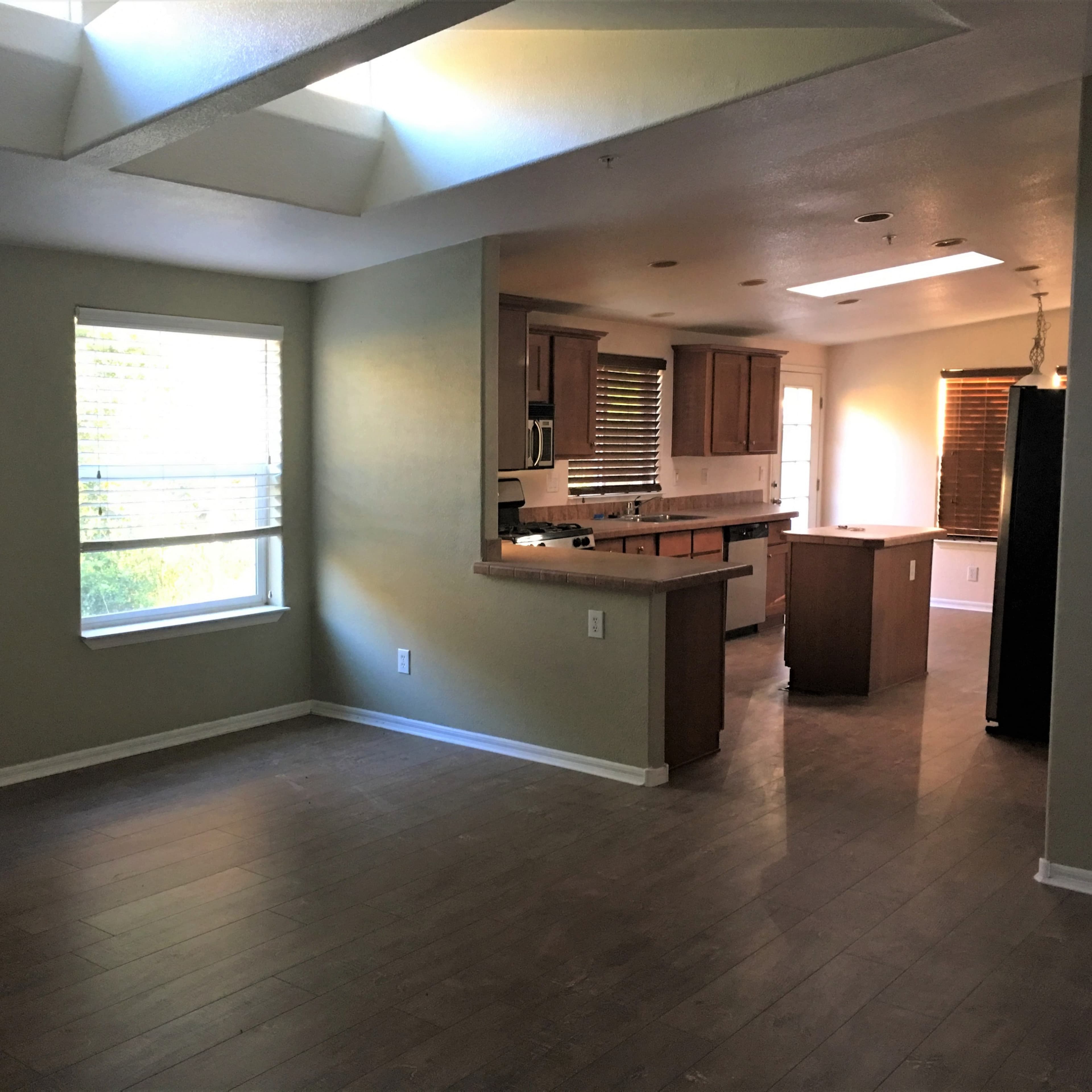 A well-lit living area transitioning into a kitchen with wooden cabinets and a central island.