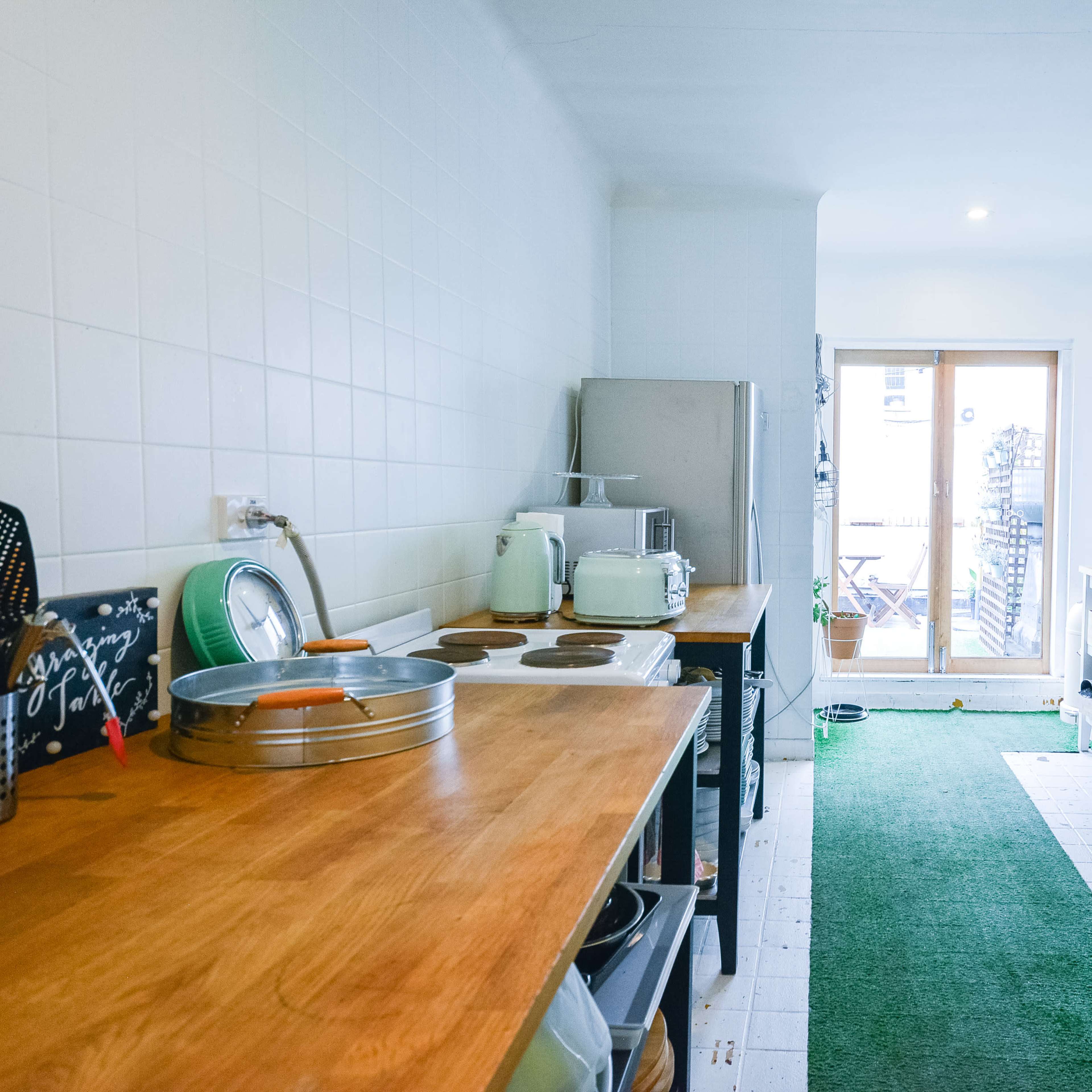 A narrow kitchen features wooden countertops, a stainless steel refrigerator, and a sliding glass door leading to a small outdoor area.