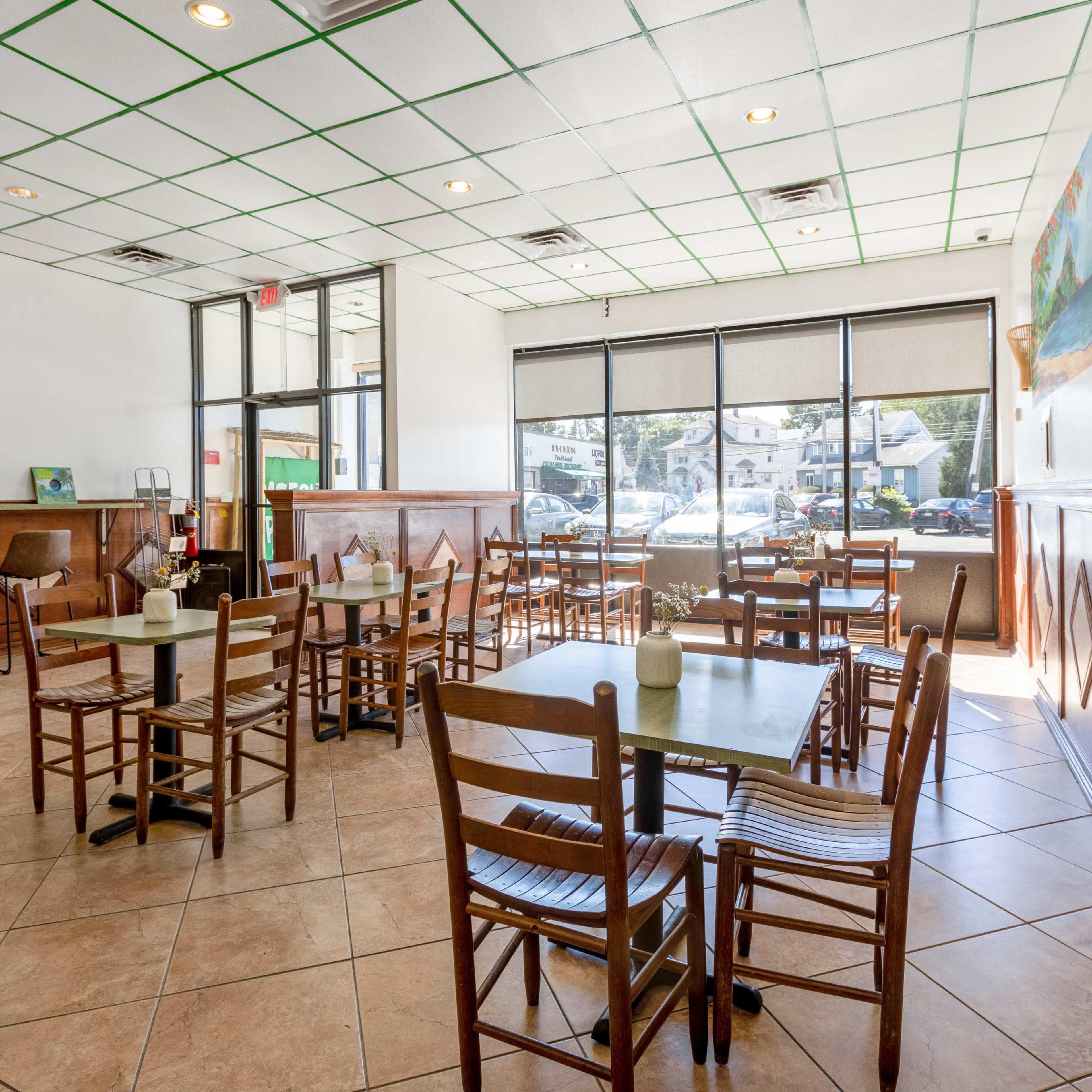 A bright, empty dining area of a restaurant with tables and chairs arranged neatly and large windows allowing natural light.