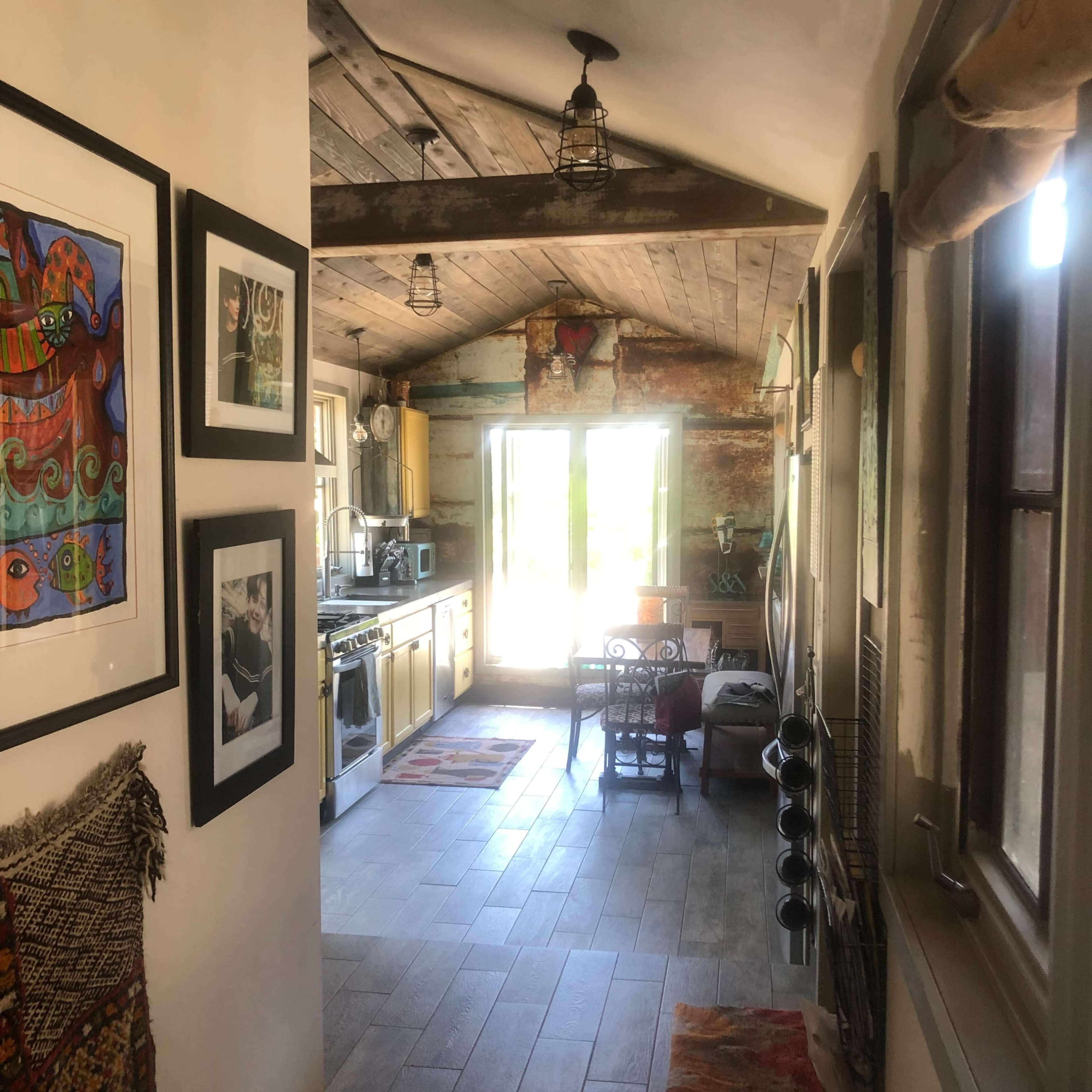 A hallway leads to a rustic kitchen with wooden beams and natural light flowing through the open door.