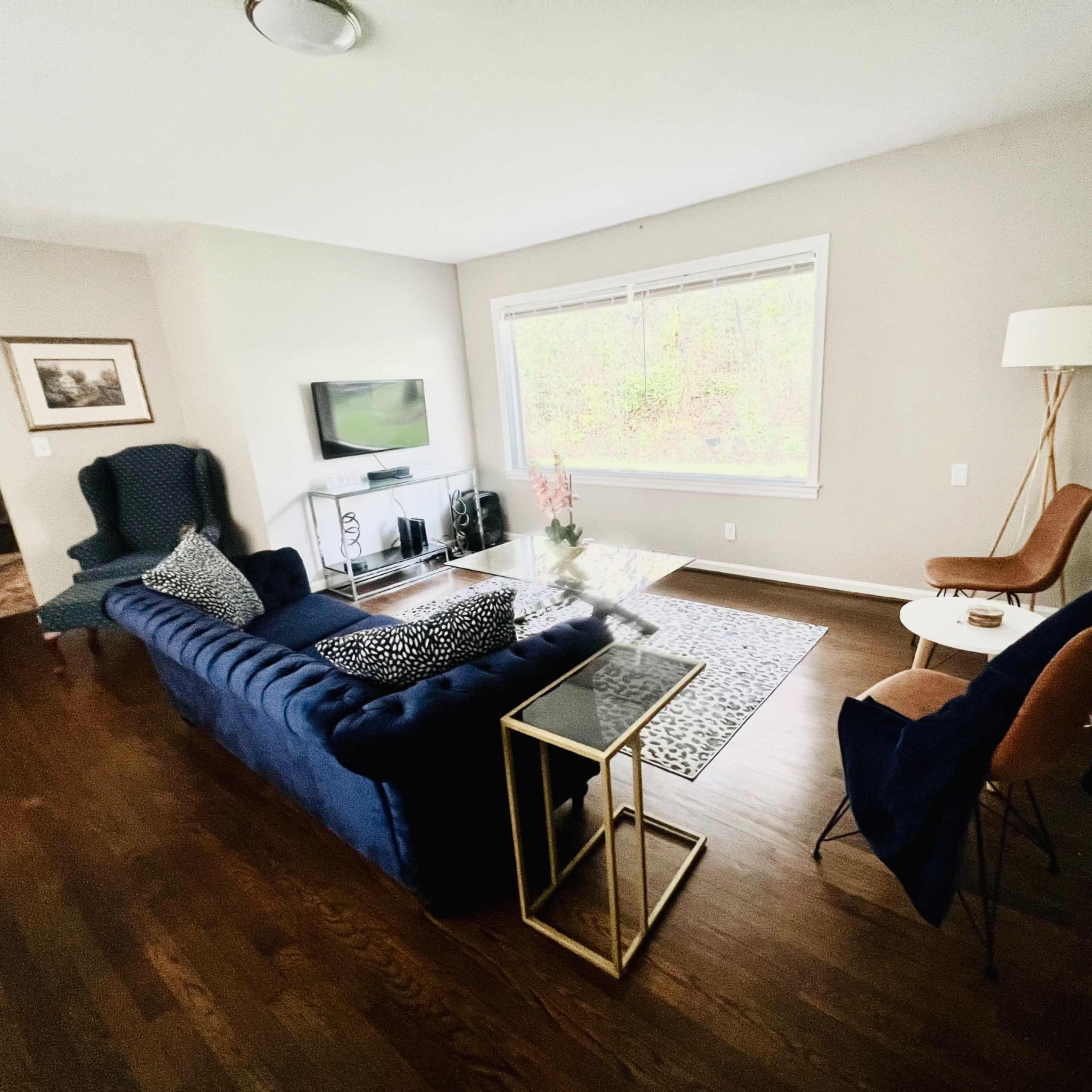 A modern living room features a blue sofa, wooden floor, television, and various furniture pieces arranged around a coffee table.