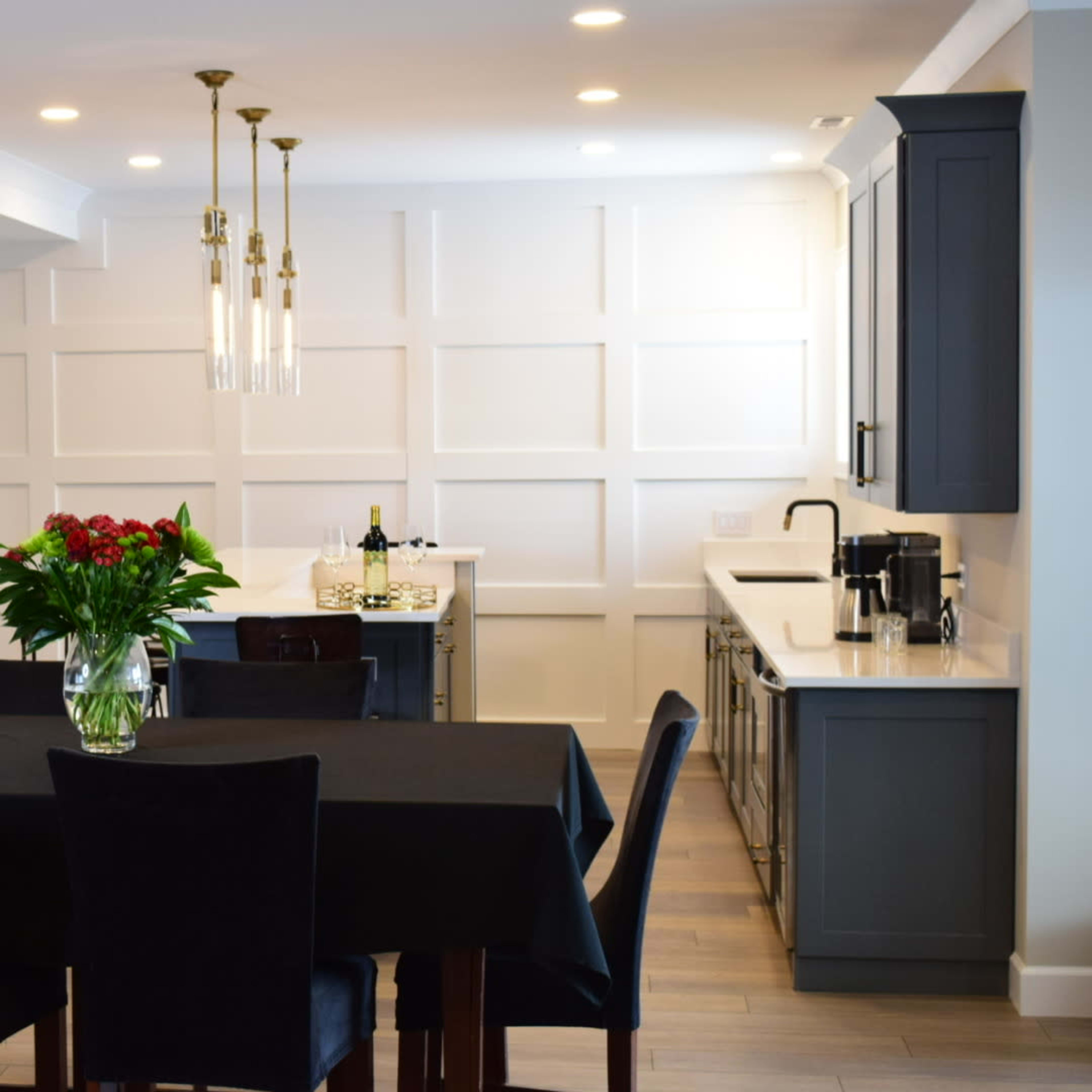 A modern dining area features a black table set with chairs, a vase of flowers, and a sleek kitchen in the background.