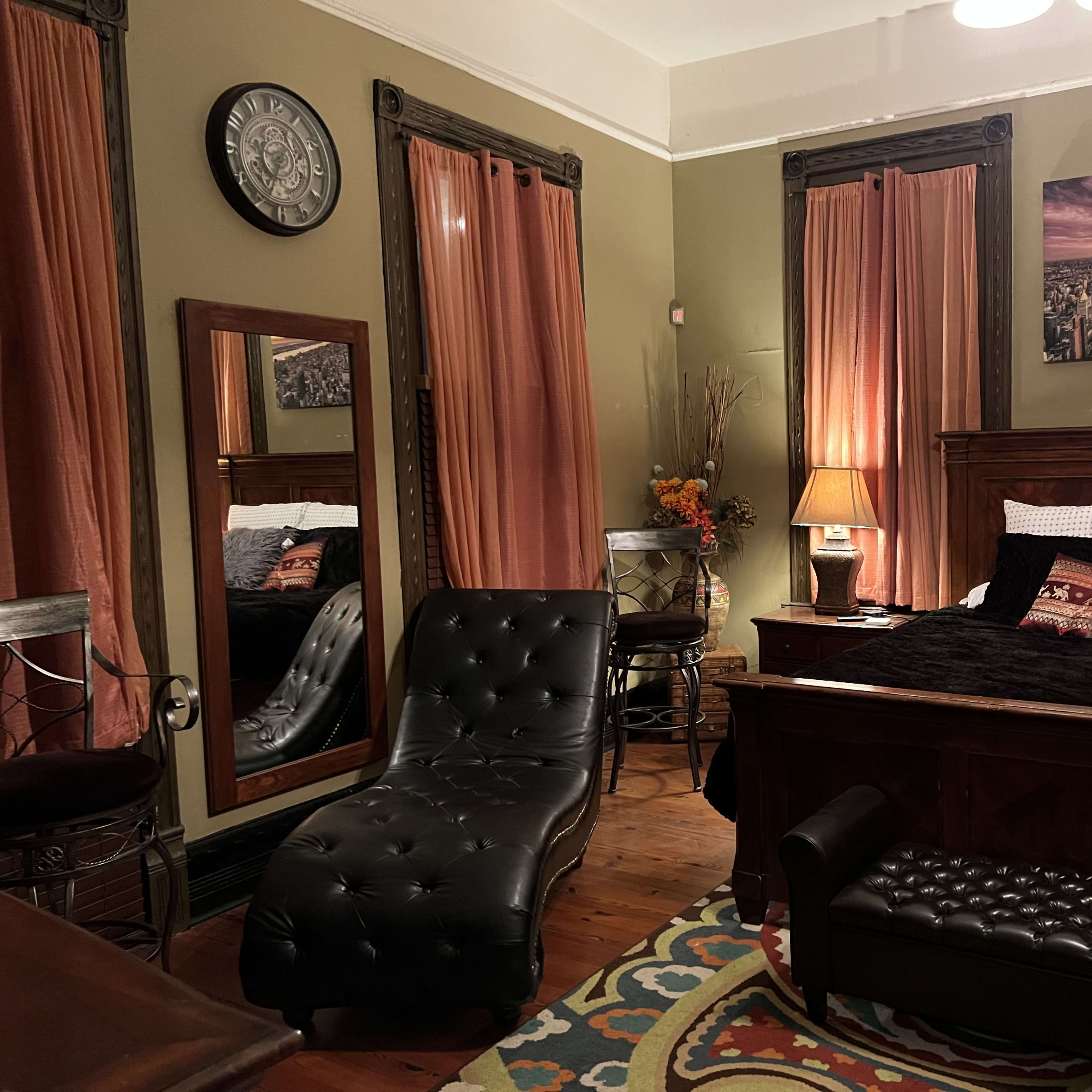A cozy bedroom featuring a dark wooden bed, a mirrored dresser, a chaise lounge, and decorative curtains.