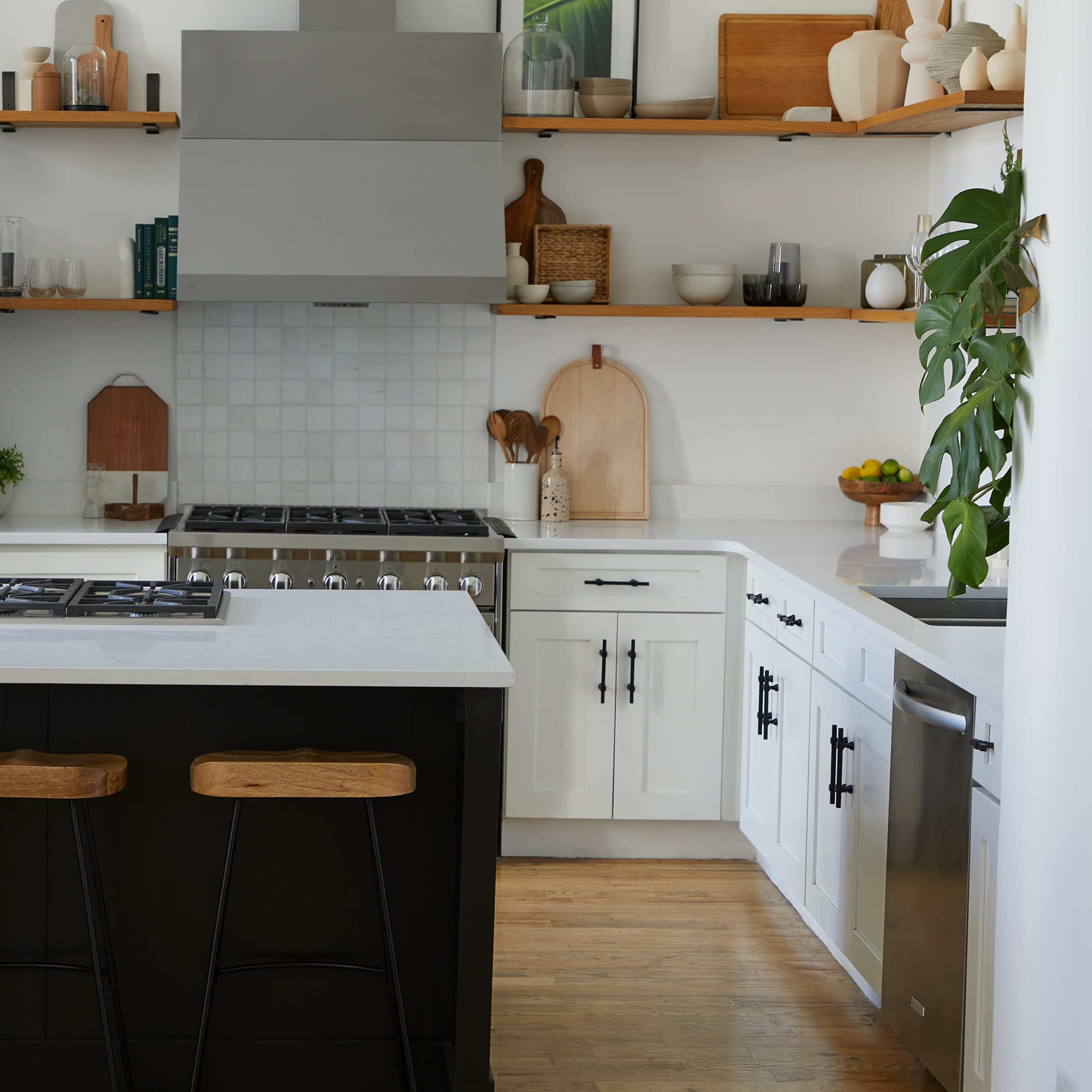A modern kitchen features white cabinets, a stainless steel refrigerator, and an island with three wooden stools.
