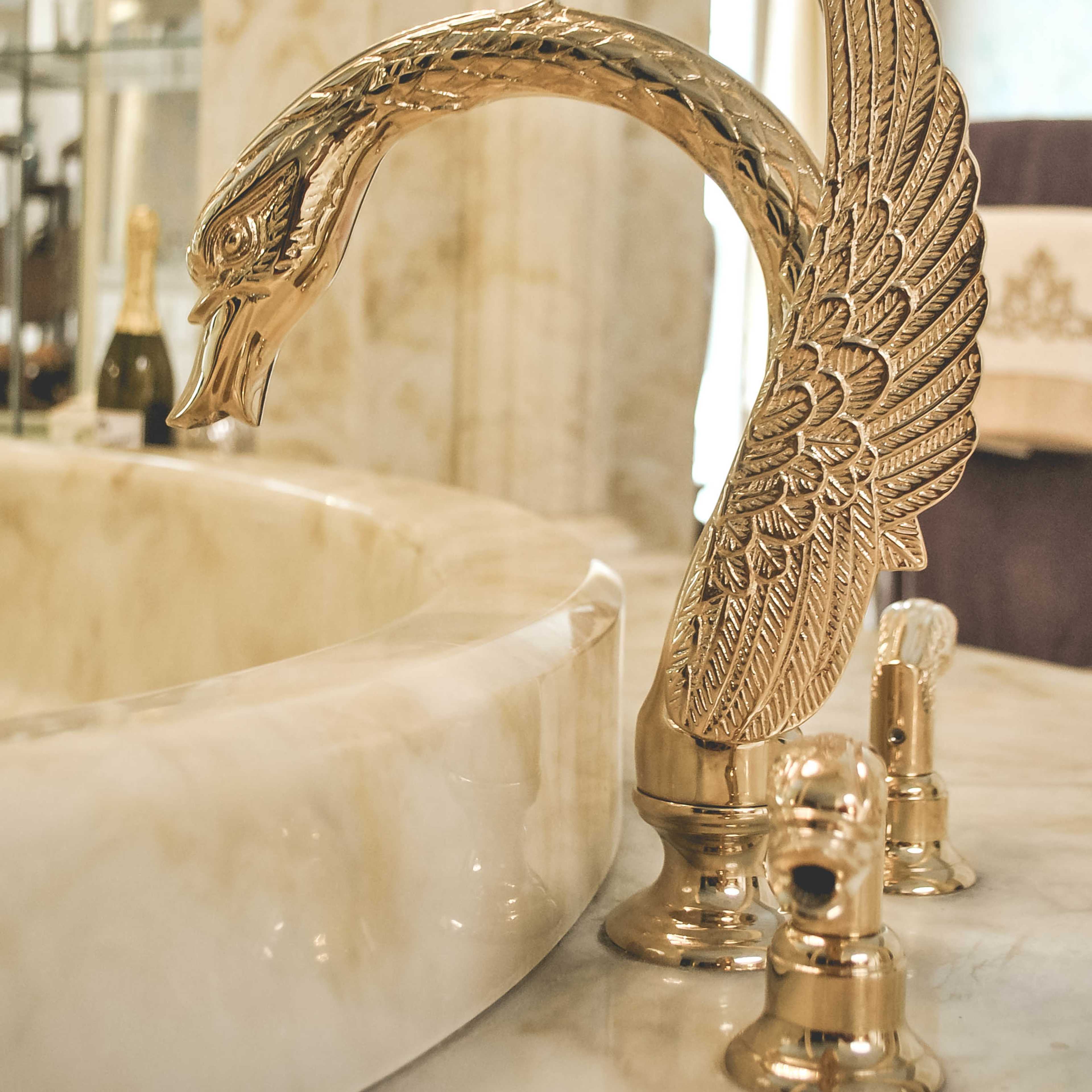 A gold-toned faucet designed in the shape of a swan, mounted on a marble sink.