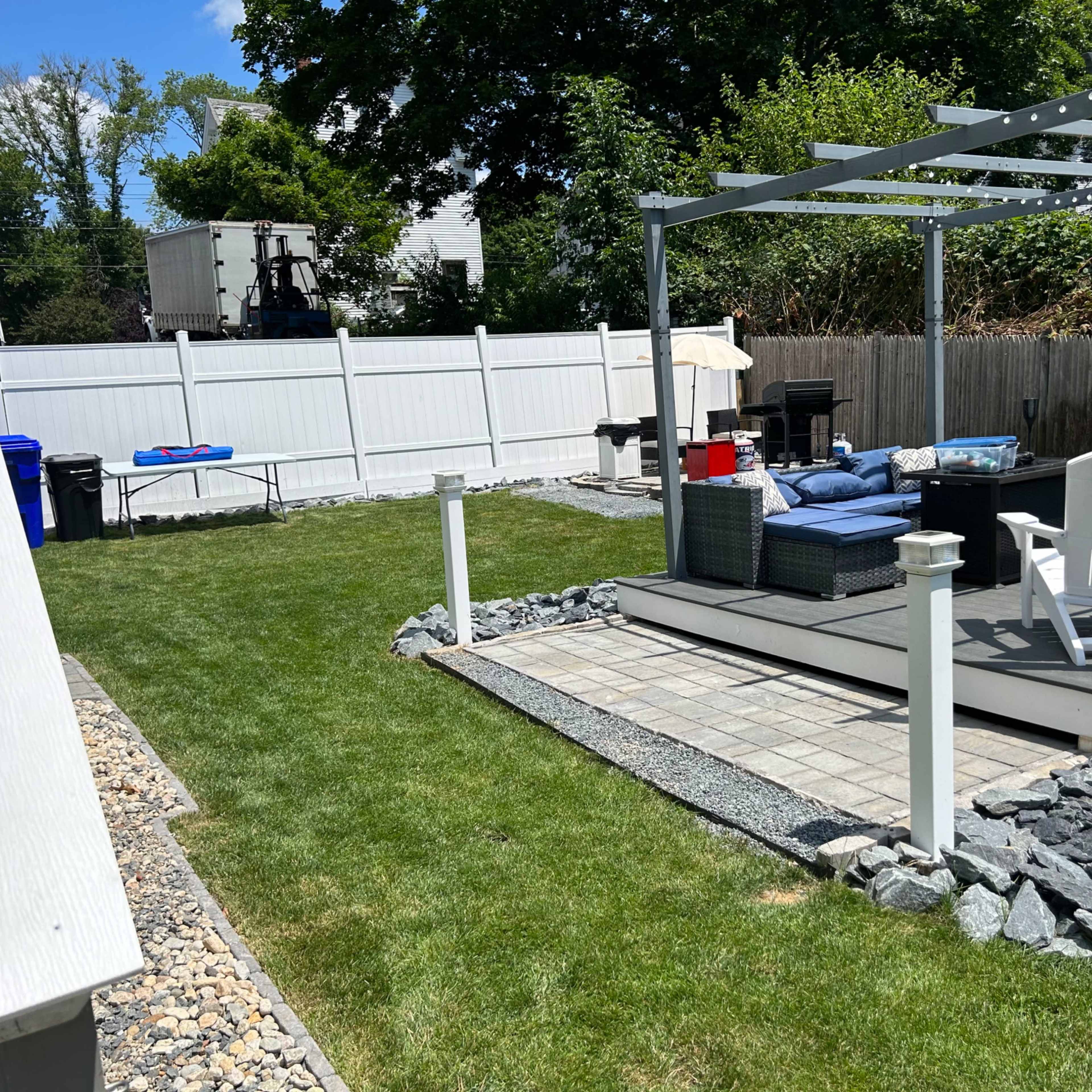 A backyard with a lawn, a stone path leading to a deck, and a covered seating area with outdoor furniture.