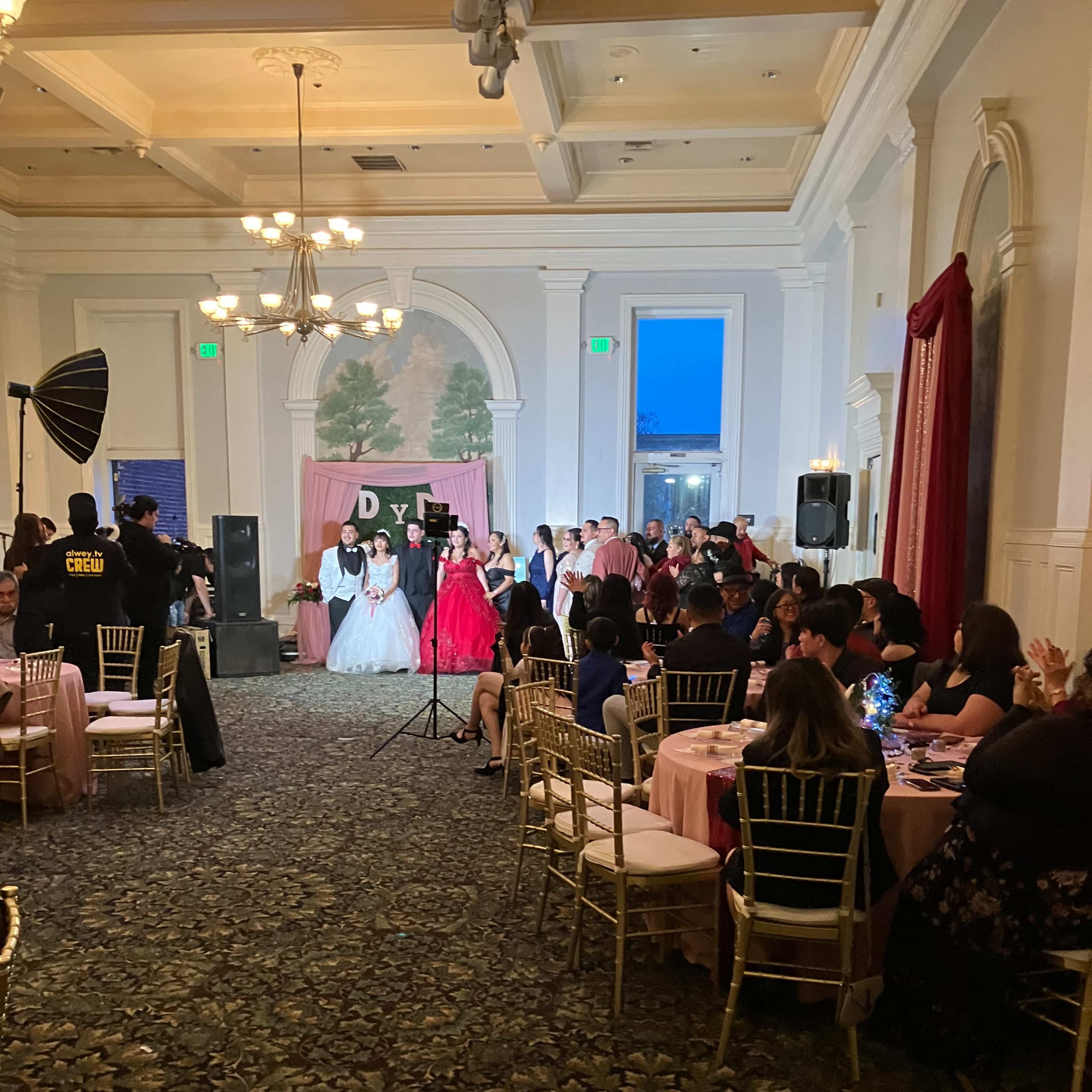 A group of people is gathered in an elegantly decorated banquet hall, celebrating a special occasion with a stage setup for speeches or performances.