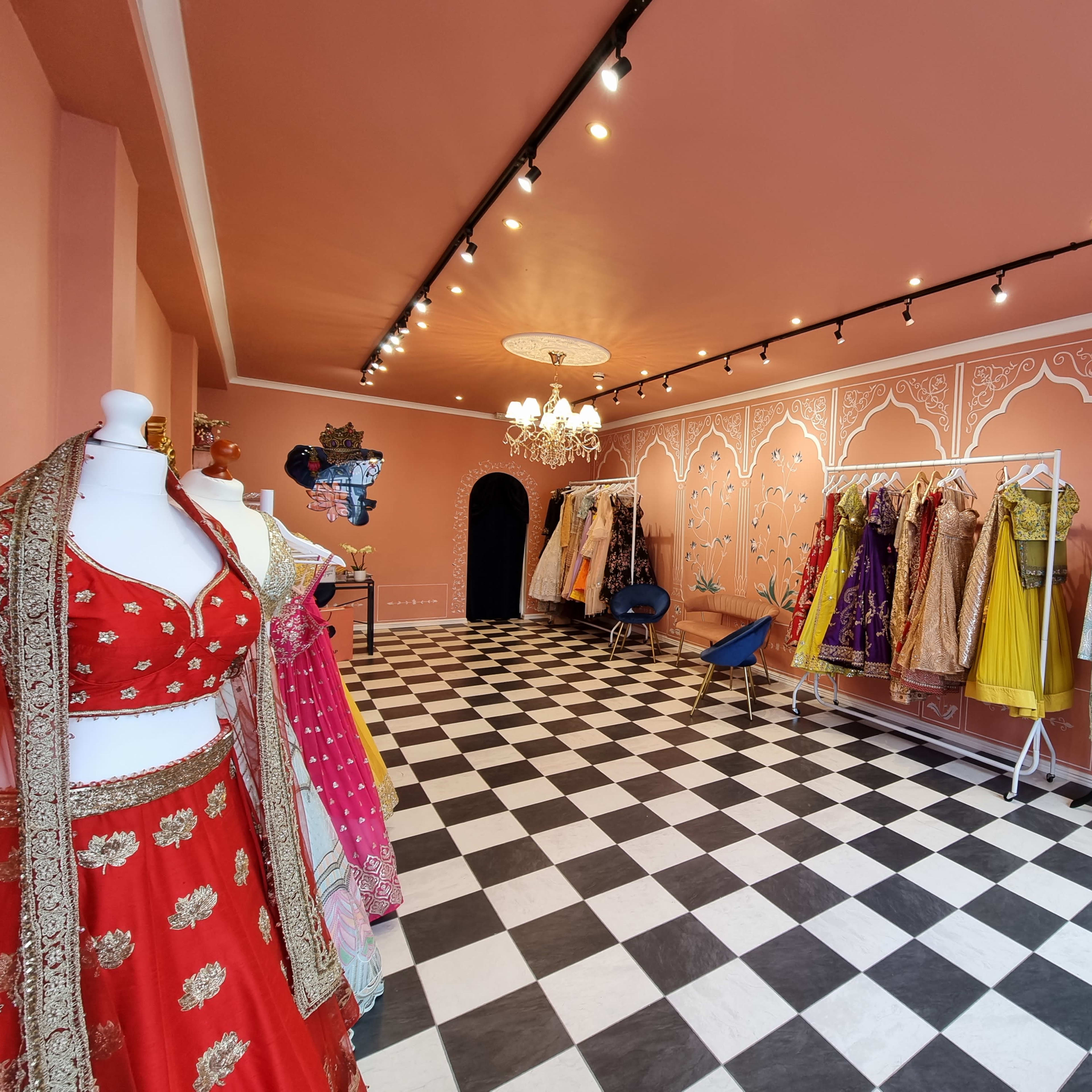 A boutique setting with a checkerboard floor, featuring colorful traditional garments displayed on racks and mannequins against a peach-colored wall.