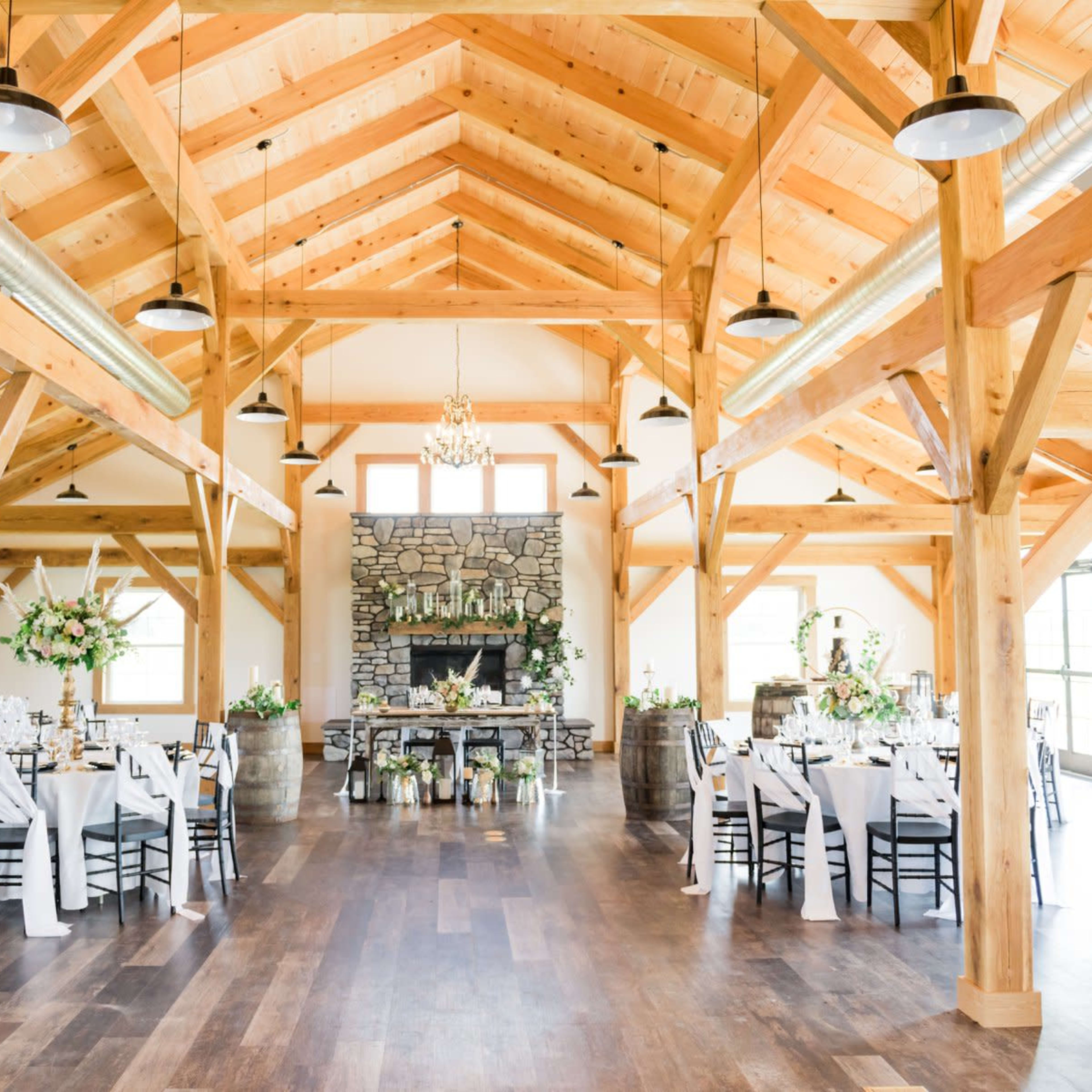 A spacious wedding reception venue featuring wooden beams, a stone fireplace, and elegantly set round tables.