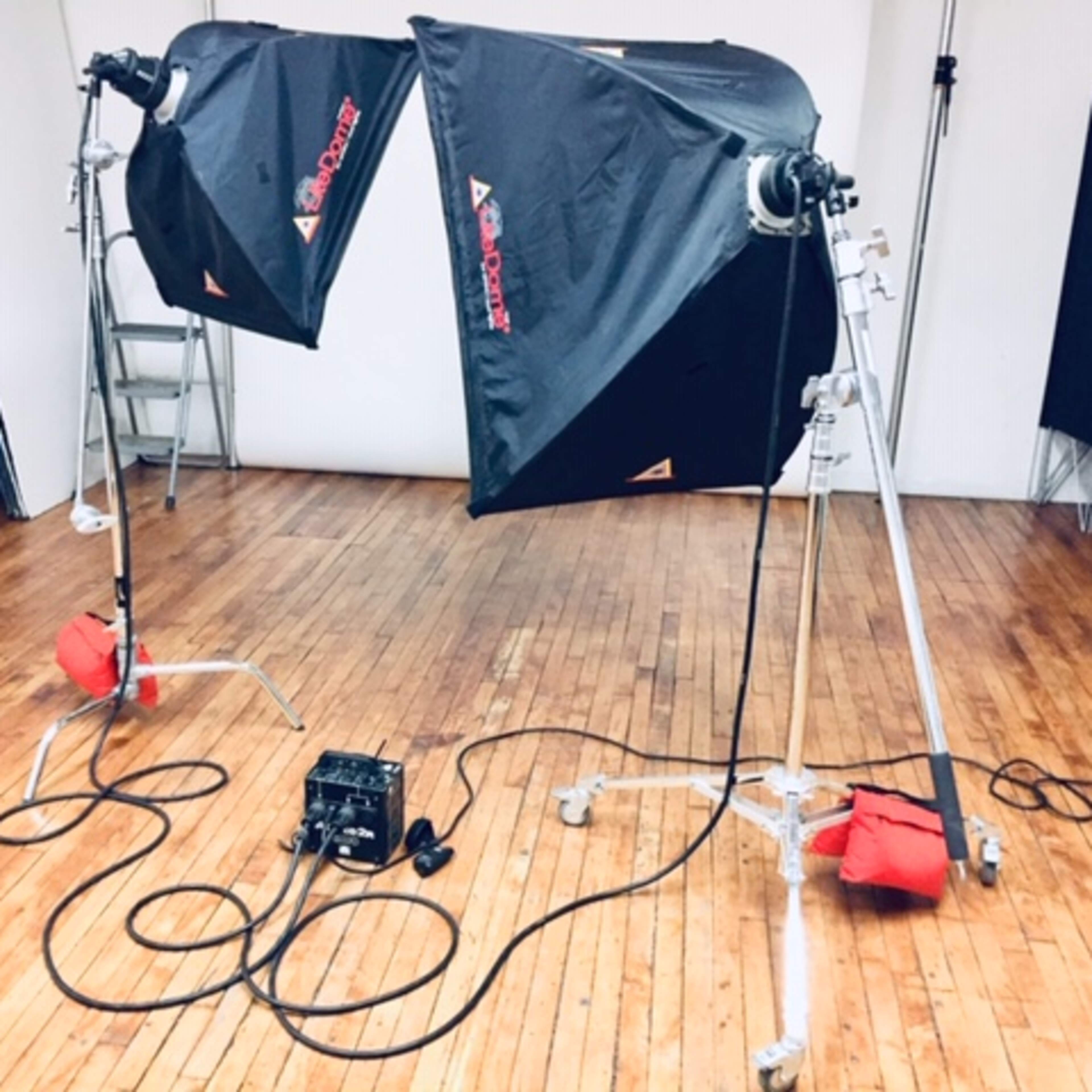 Two studio lights on stands with a power source and cables scattered on a wooden floor.