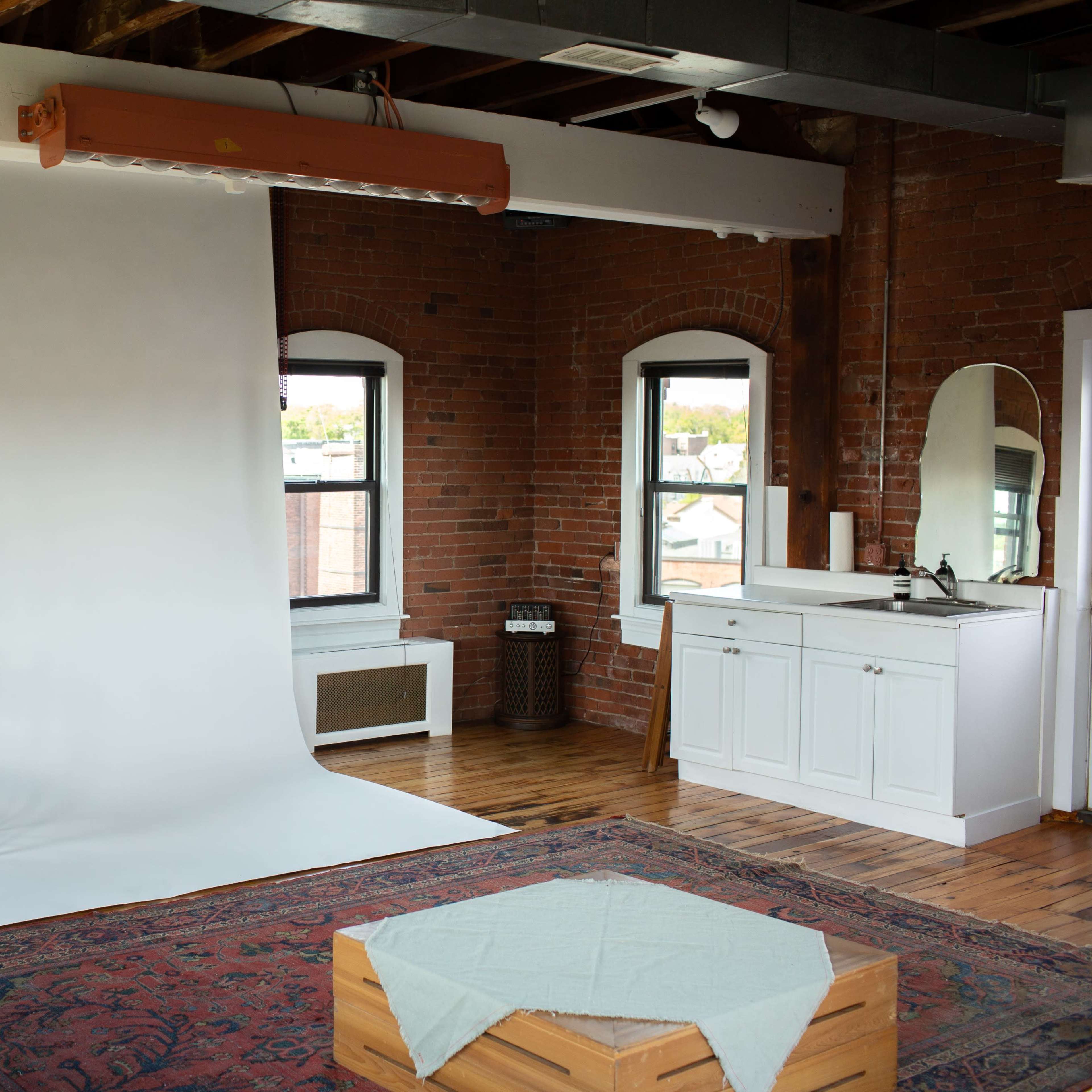 A bright studio space with a white backdrop, a single wooden chair, large windows, and a wooden floor.