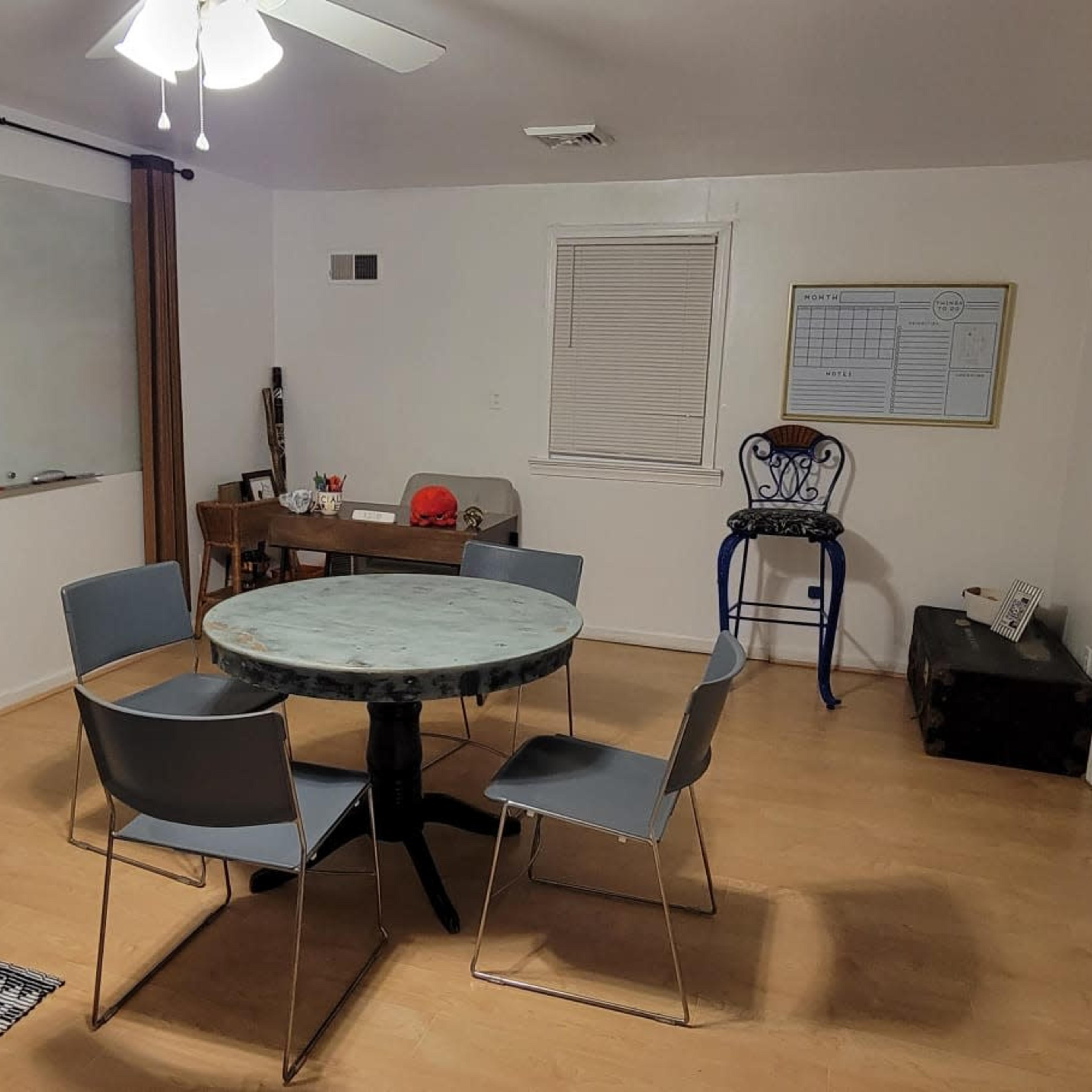 A simple room with a round table surrounded by six chairs, a wall-mounted mirror, and a large mural of a train on one wall.