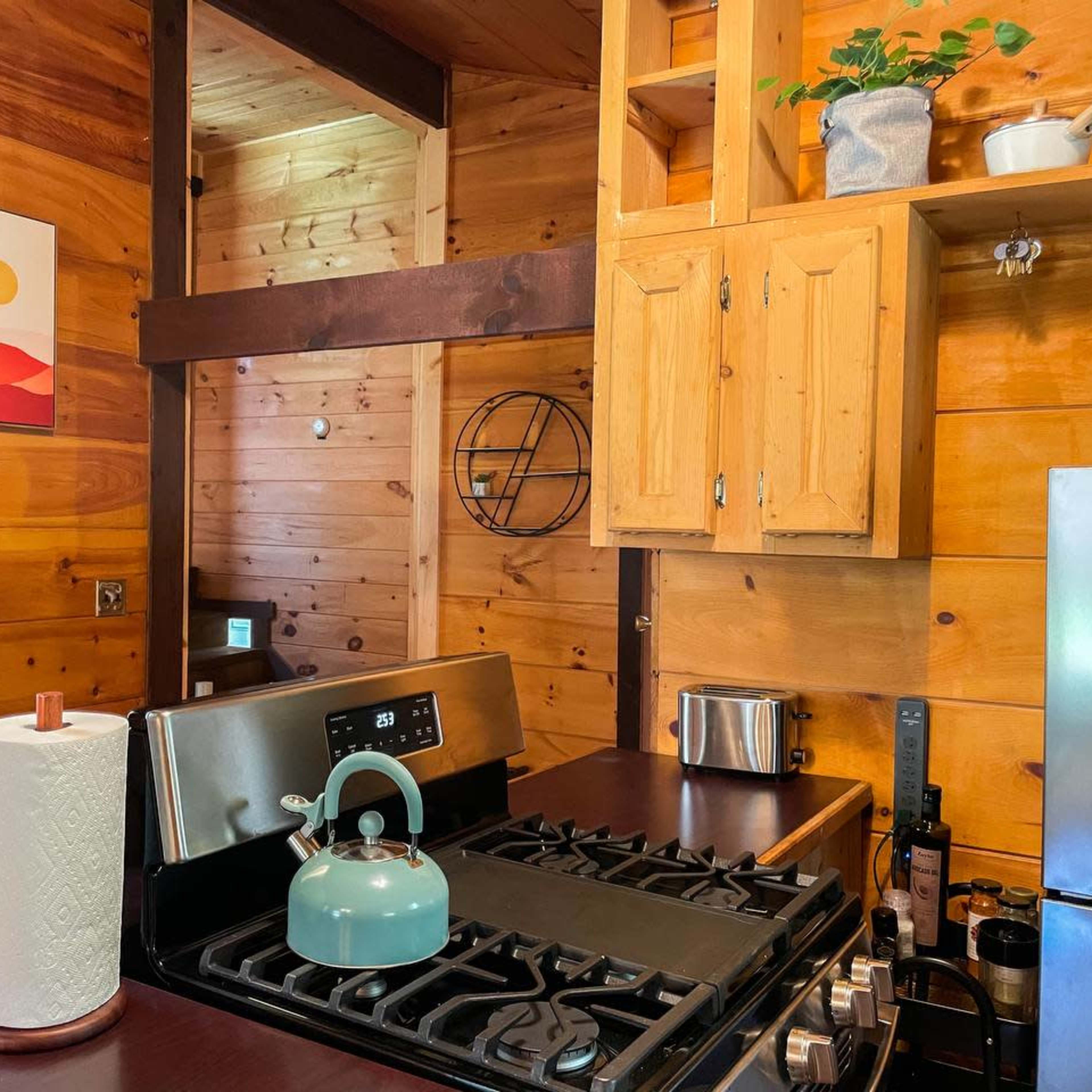 A wooden kitchen with a gas stove, cabinets, and a green kettle on the countertop.