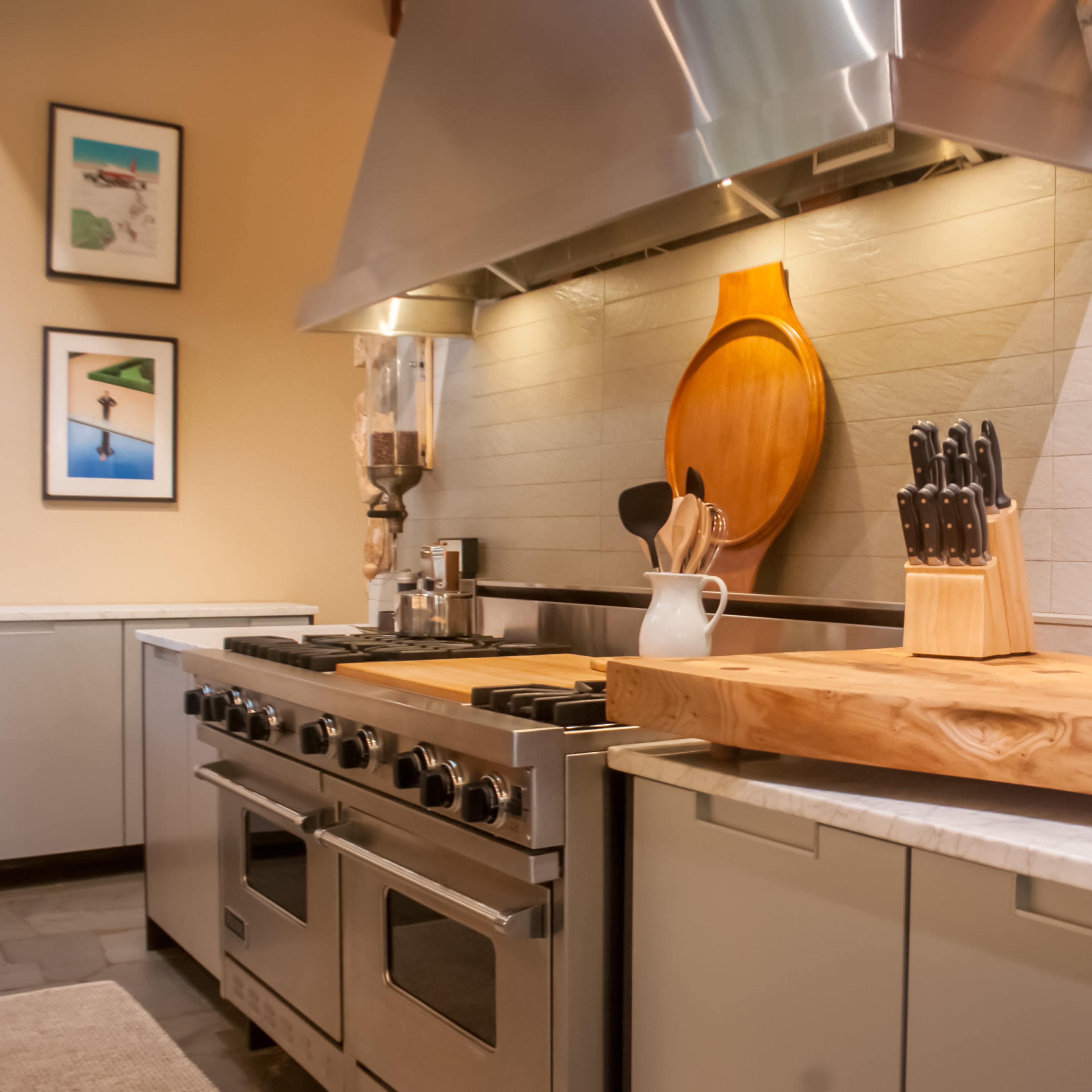 A modern kitchen featuring a large wooden cutting board, a knife block, a stainless steel stove, and stone wall accents.