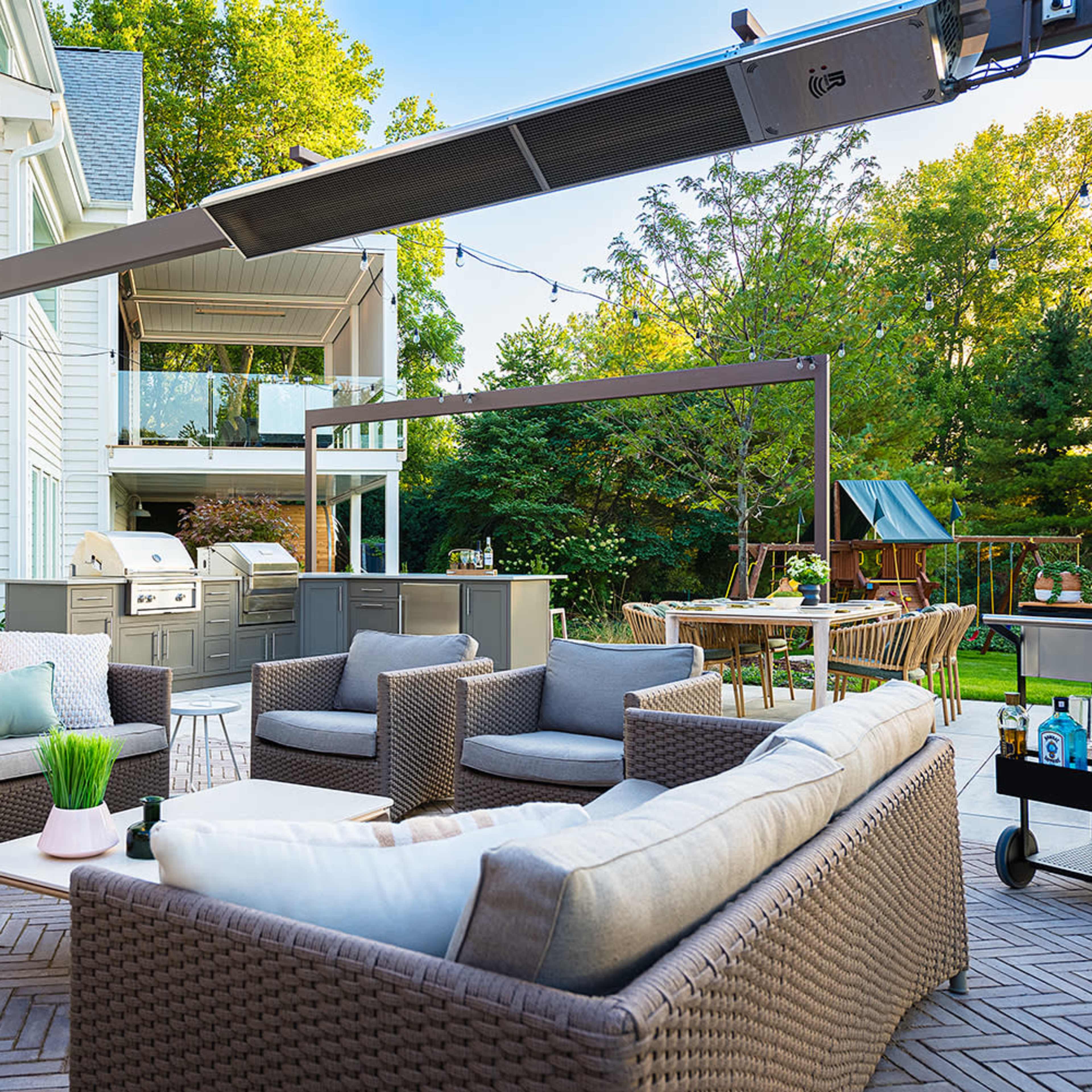An outdoor patio with wicker furniture, a grill, and a dining area surrounded by greenery.