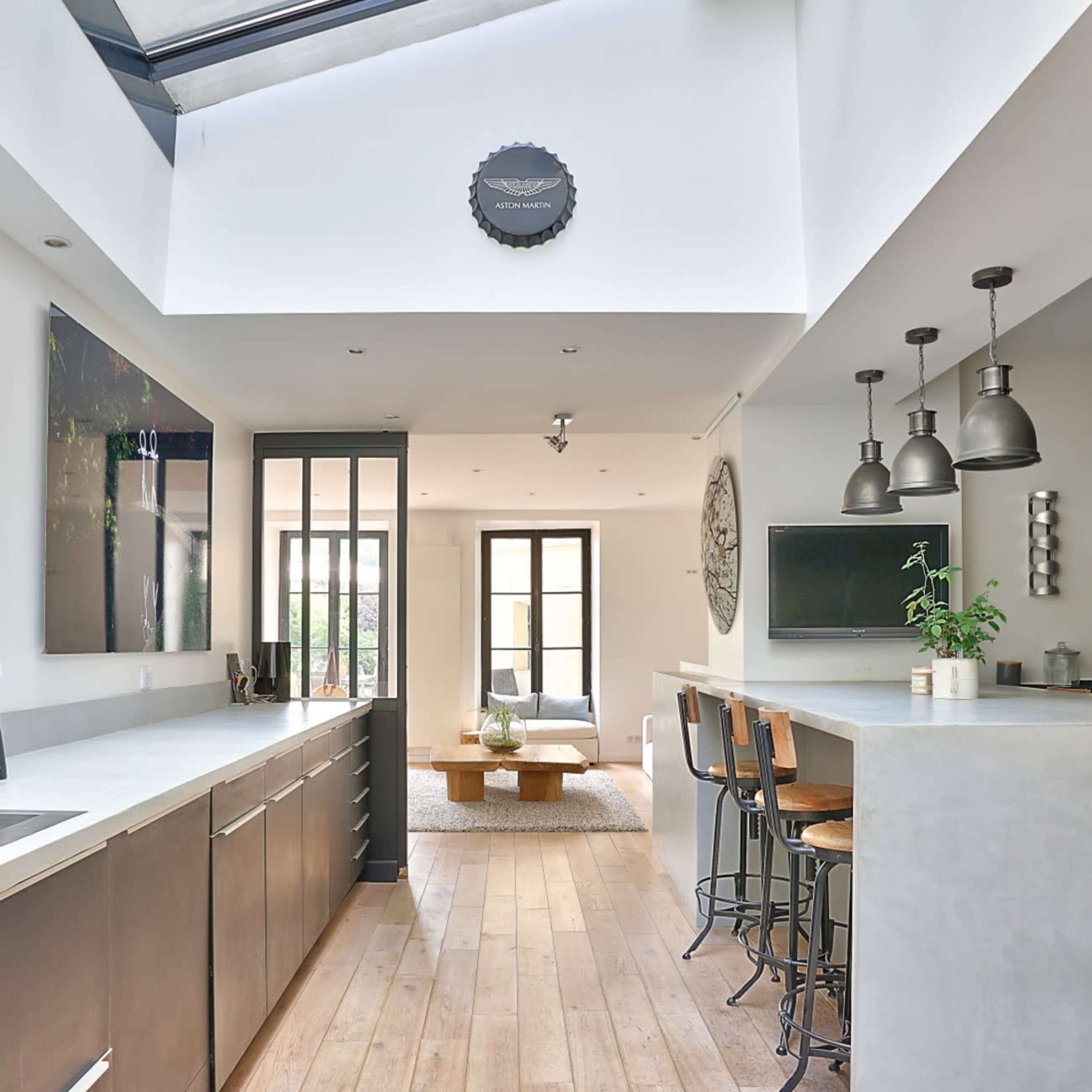A modern kitchen with a linear design features a central island, sleek cabinetry, and large windows allowing natural light to enter.