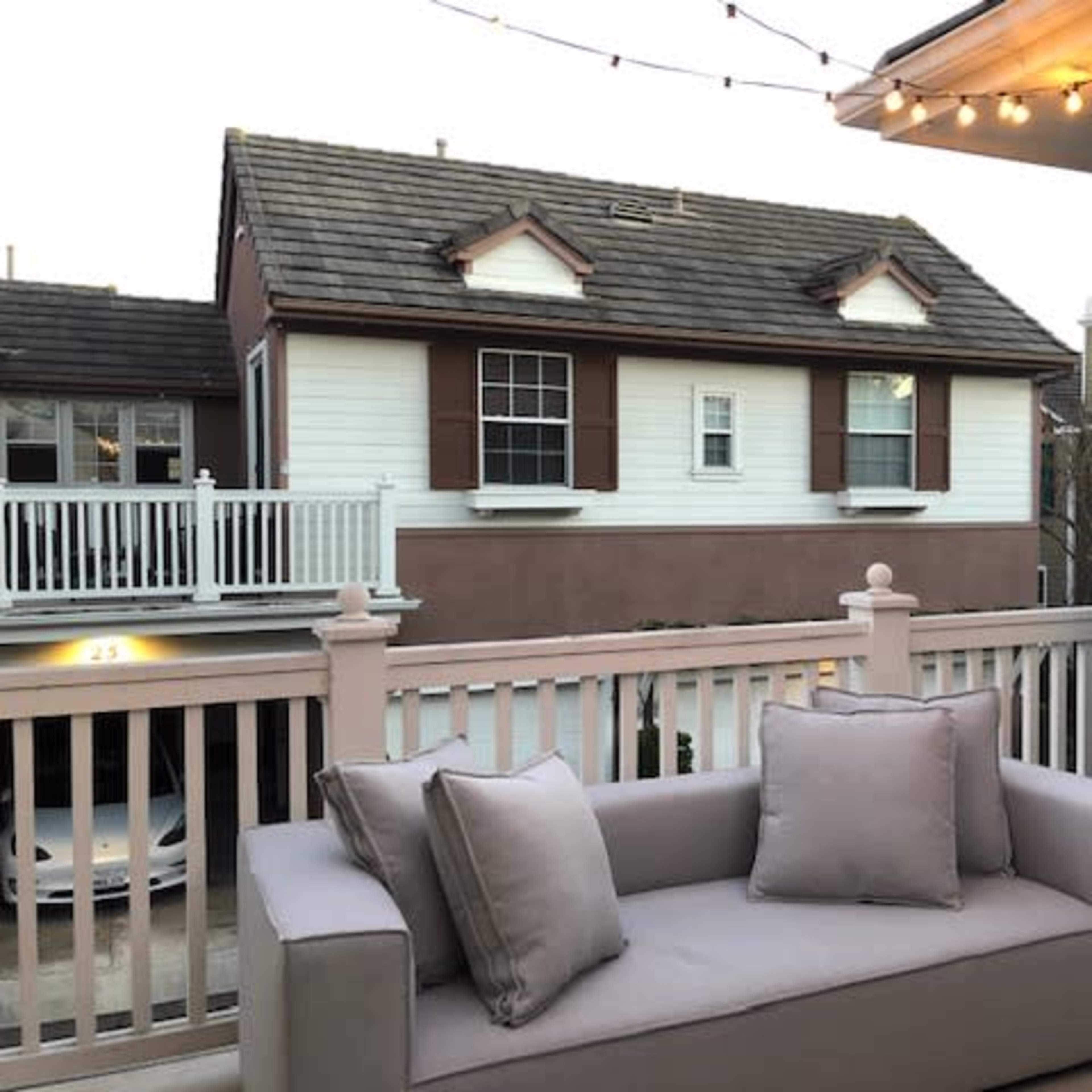 A gray sofa with cushions is situated on a balcony, overlooking a neighboring building with decorative shutters and a sloped roof.