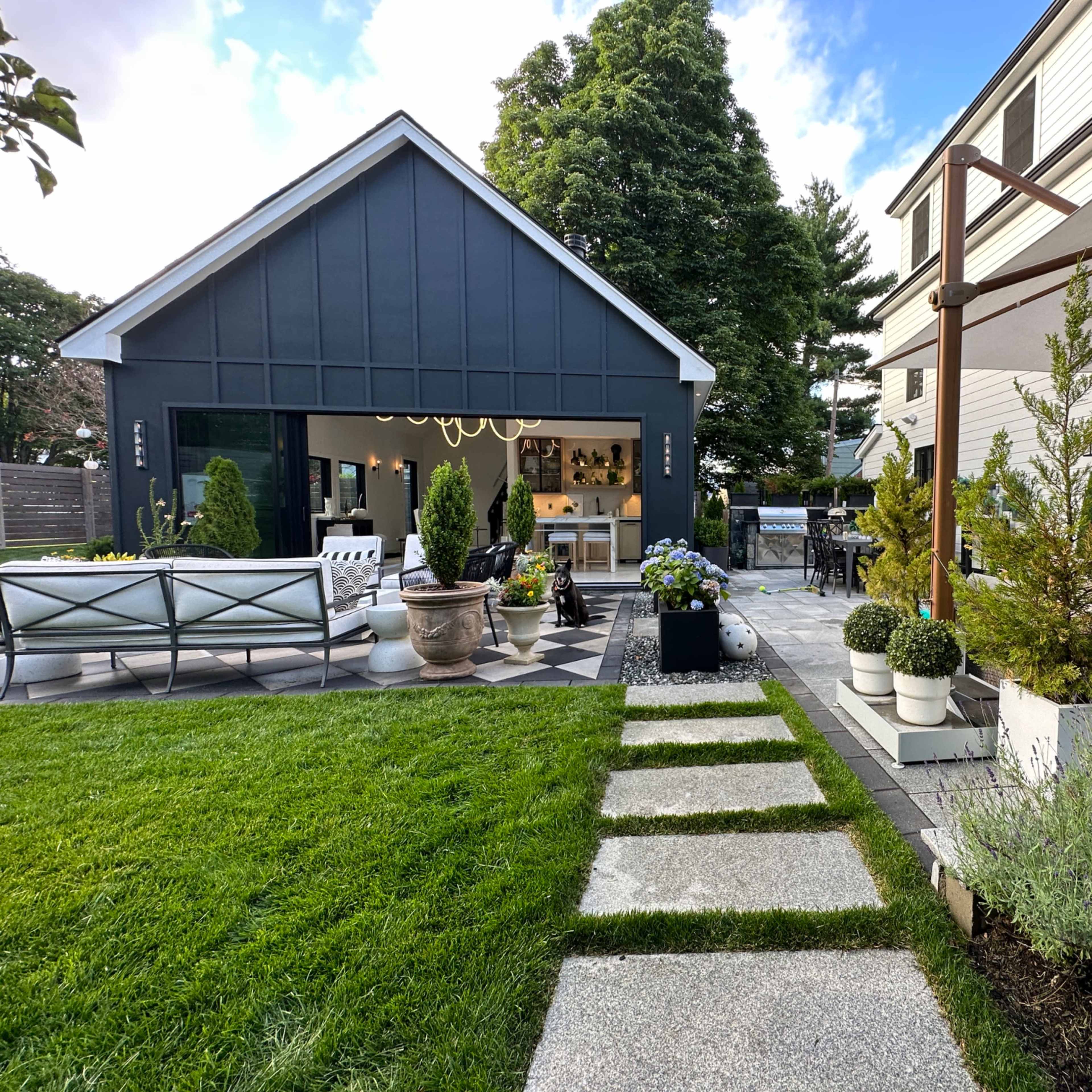 A landscaped backyard featuring a stone pathway leading to a modern shed, surrounded by greenery and outdoor furniture.