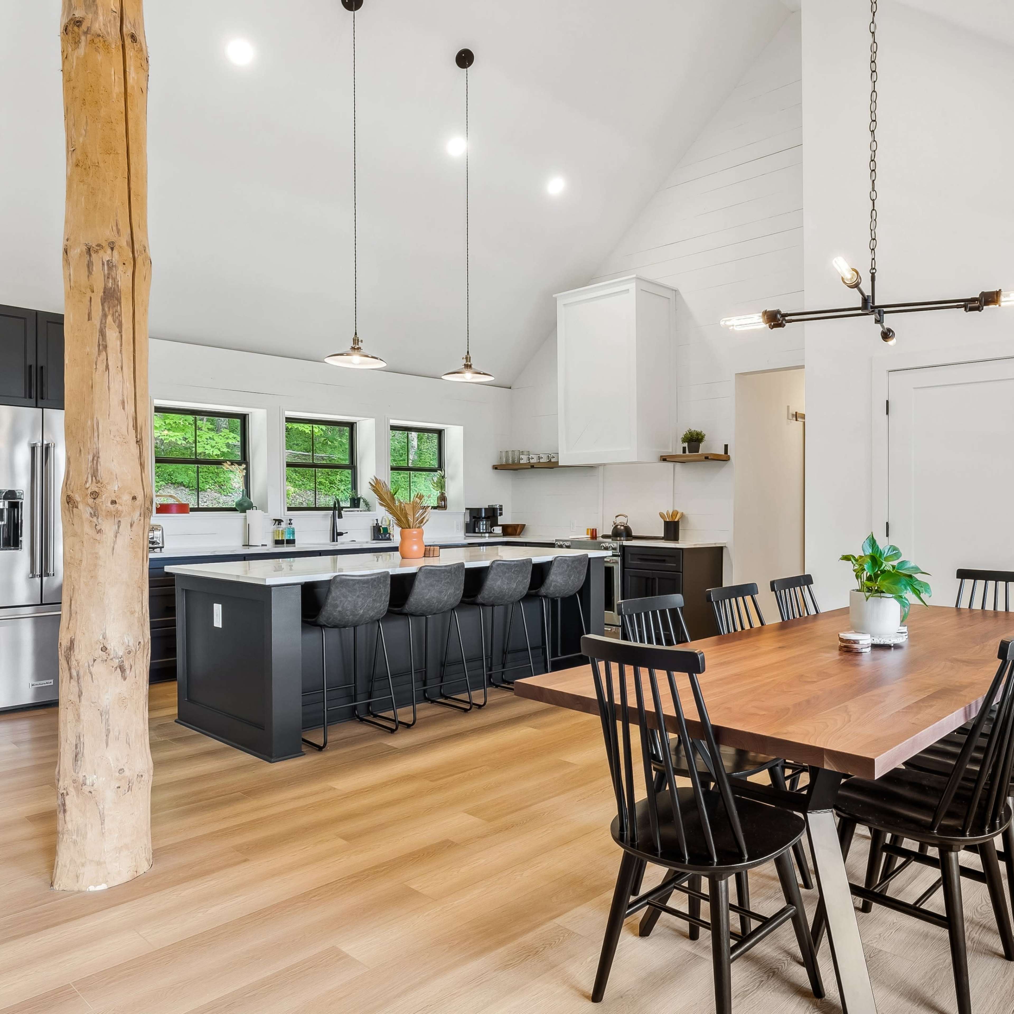 A modern kitchen and dining area with a long wooden table, black chairs, and a large kitchen island with bar stools.