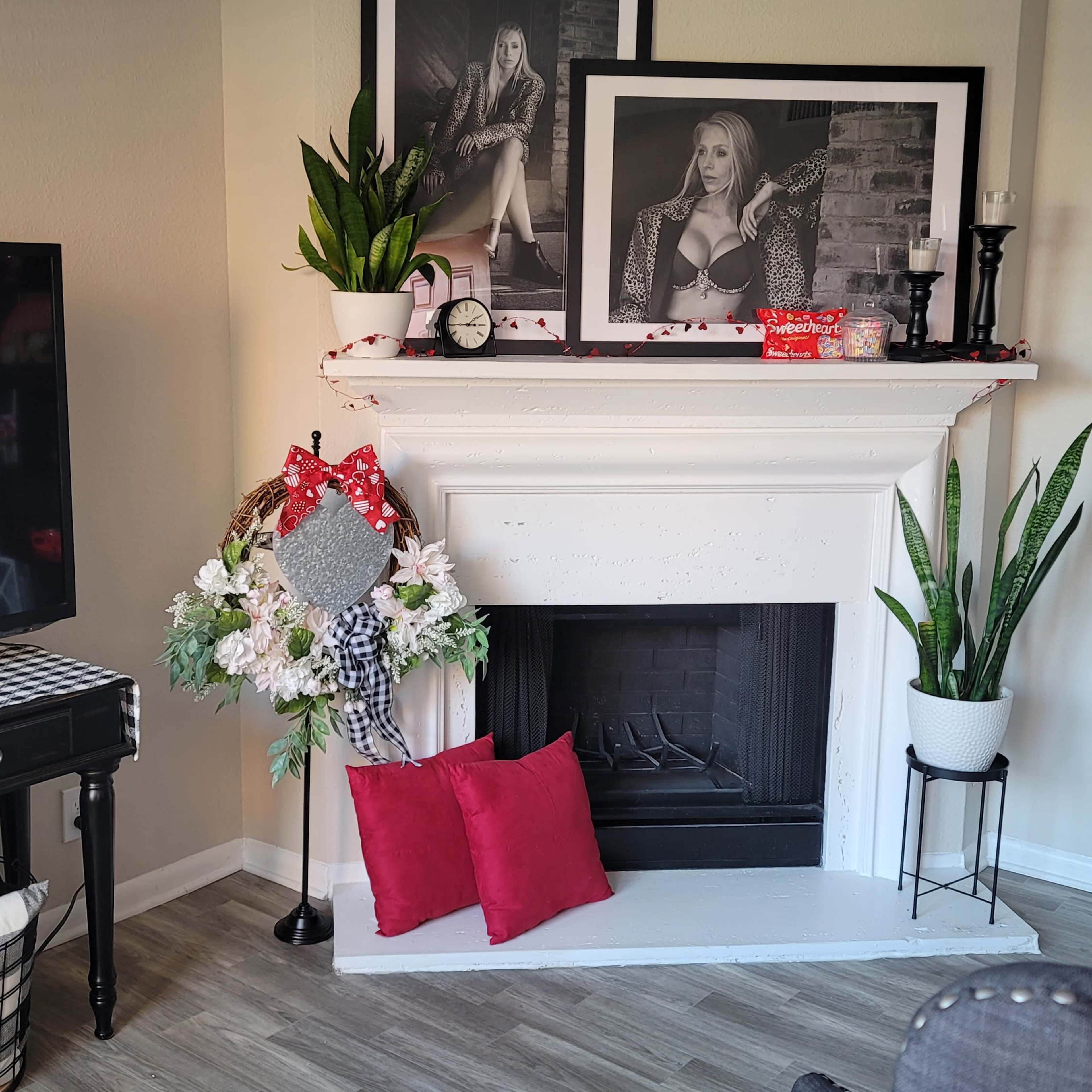 The scene features a living room corner with a black television, a decorated fireplace, a floral wreath, and a sofa with red cushions.