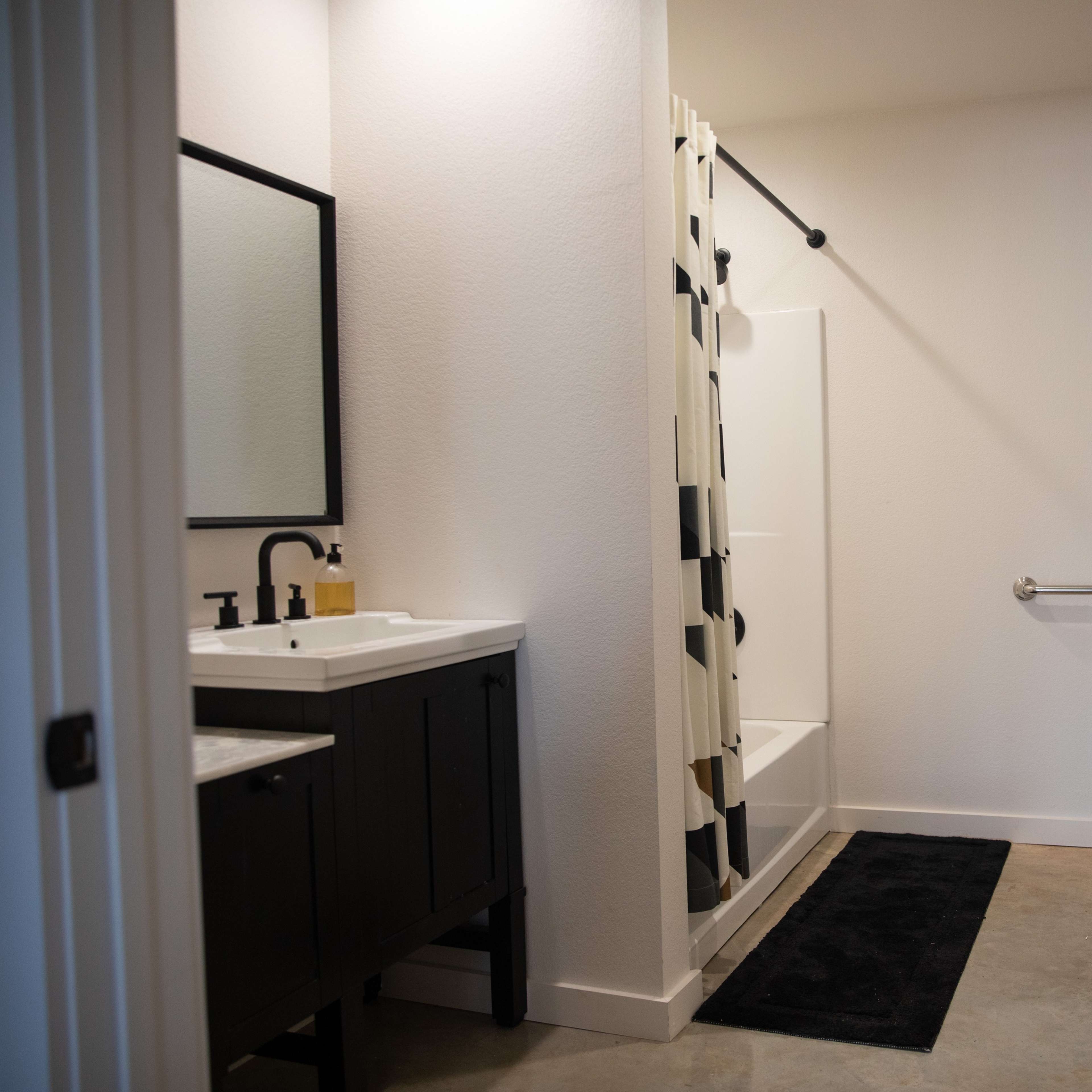 A modern bathroom featuring a shower, toilet, sink with a cabinet, and a dark rug on the floor.