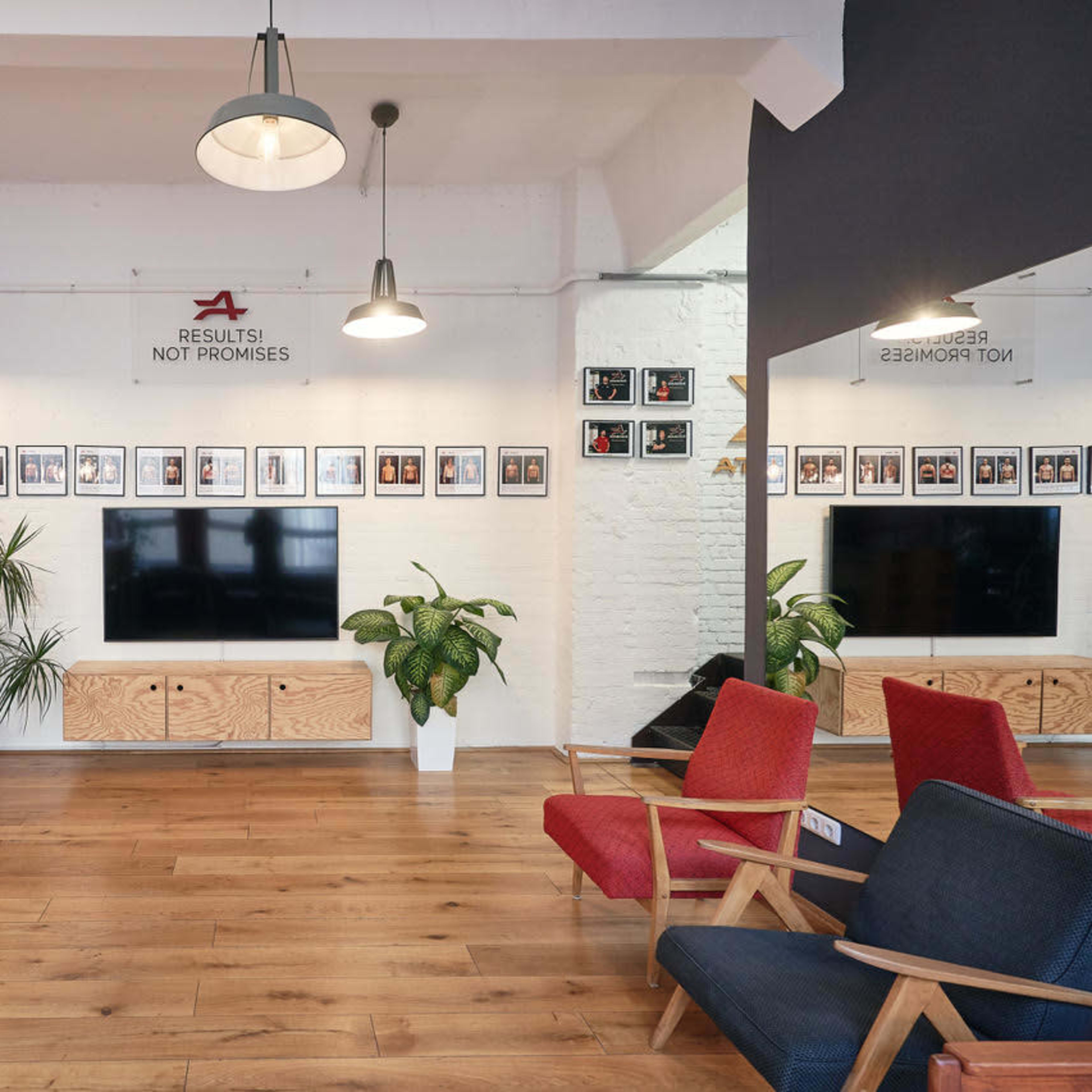 A modern office reception area with a television, framed photos on the wall, potted plants, and seating arrangements.