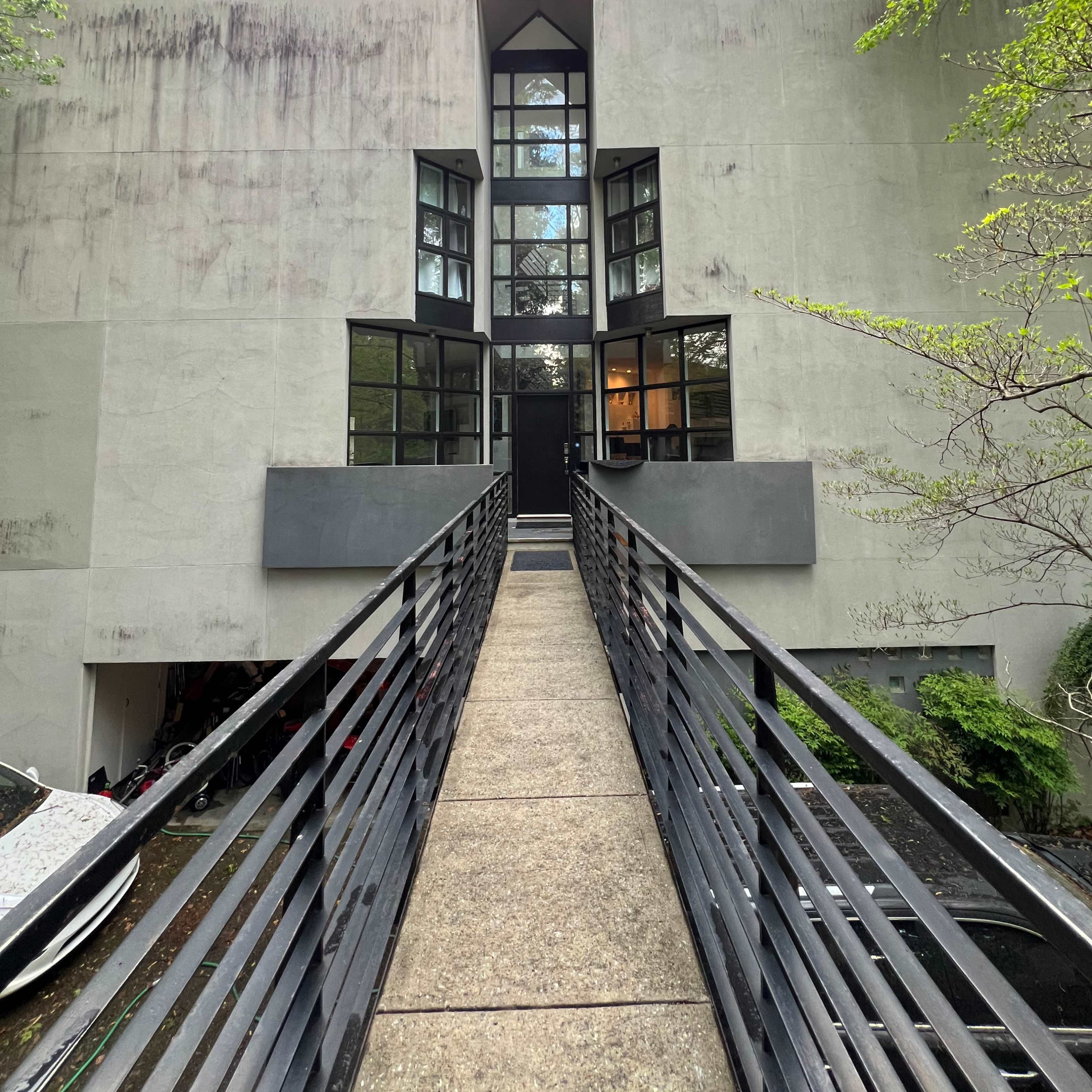 A modern, minimalist building with a gray facade, large windows, and a walkway leading to the entrance.