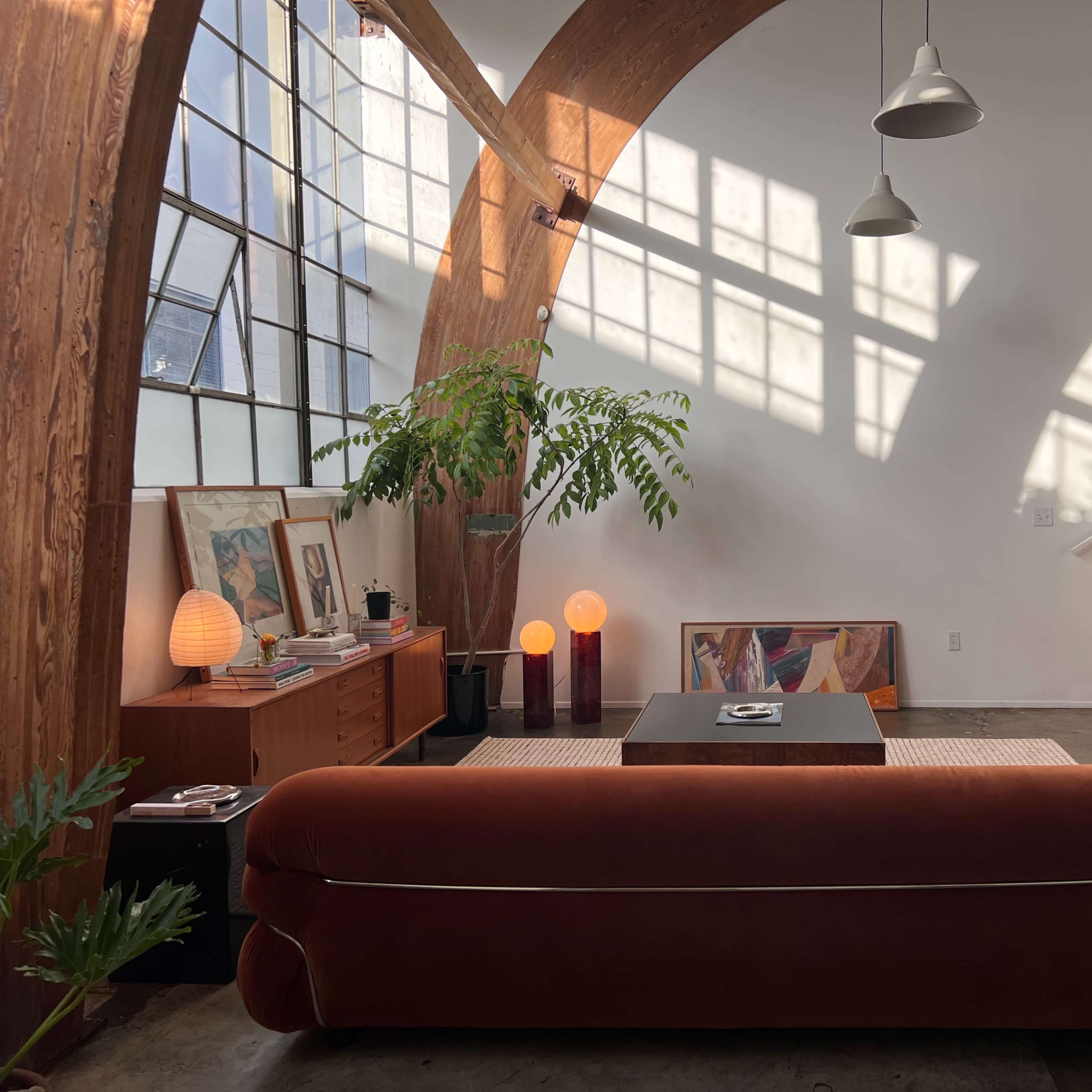A modern living room featuring a brown sofa, a coffee table, and large windows that cast shadows on the walls.
