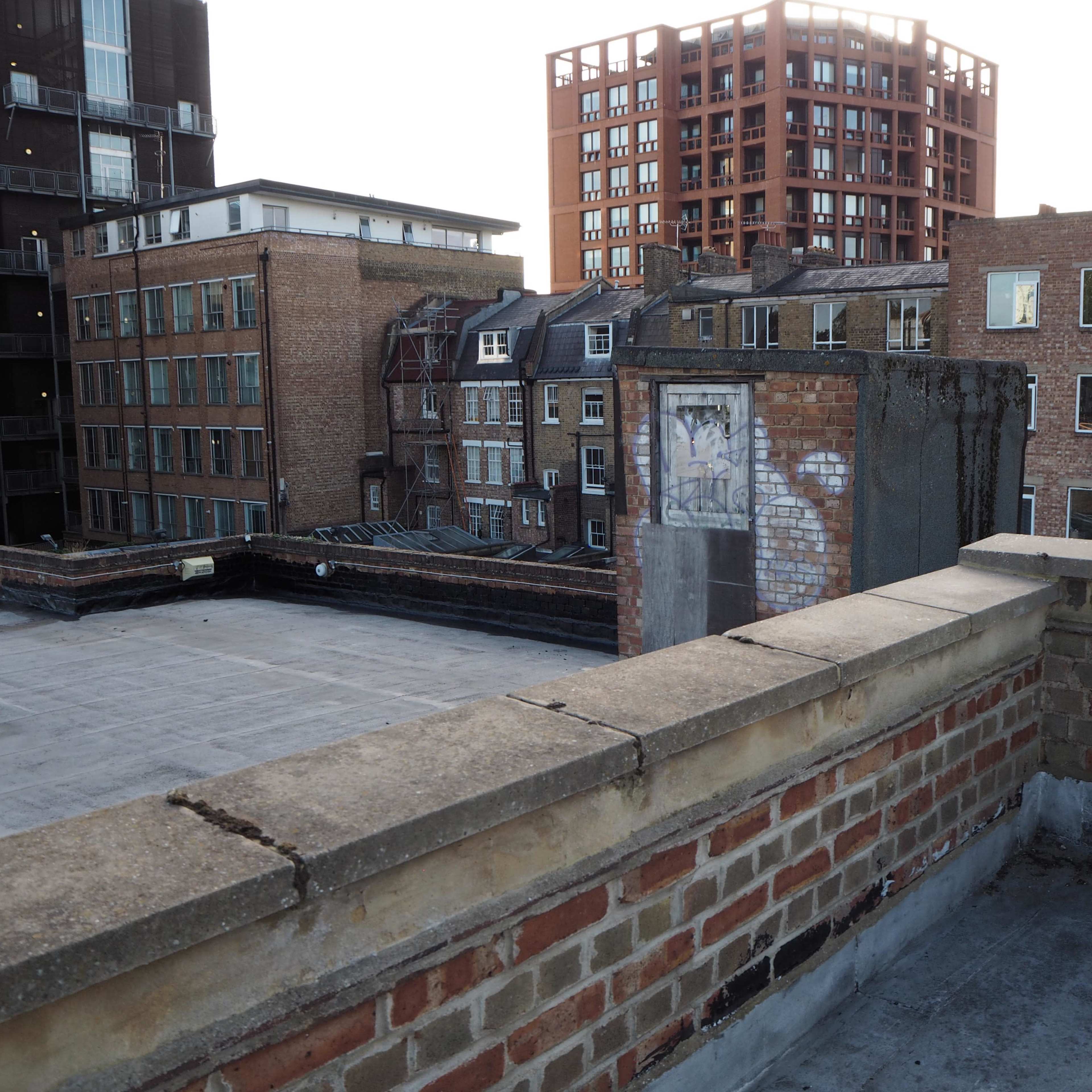 A rooftop view overlooking a cityscape with buildings featuring brick facades and a mural on one of the walls.