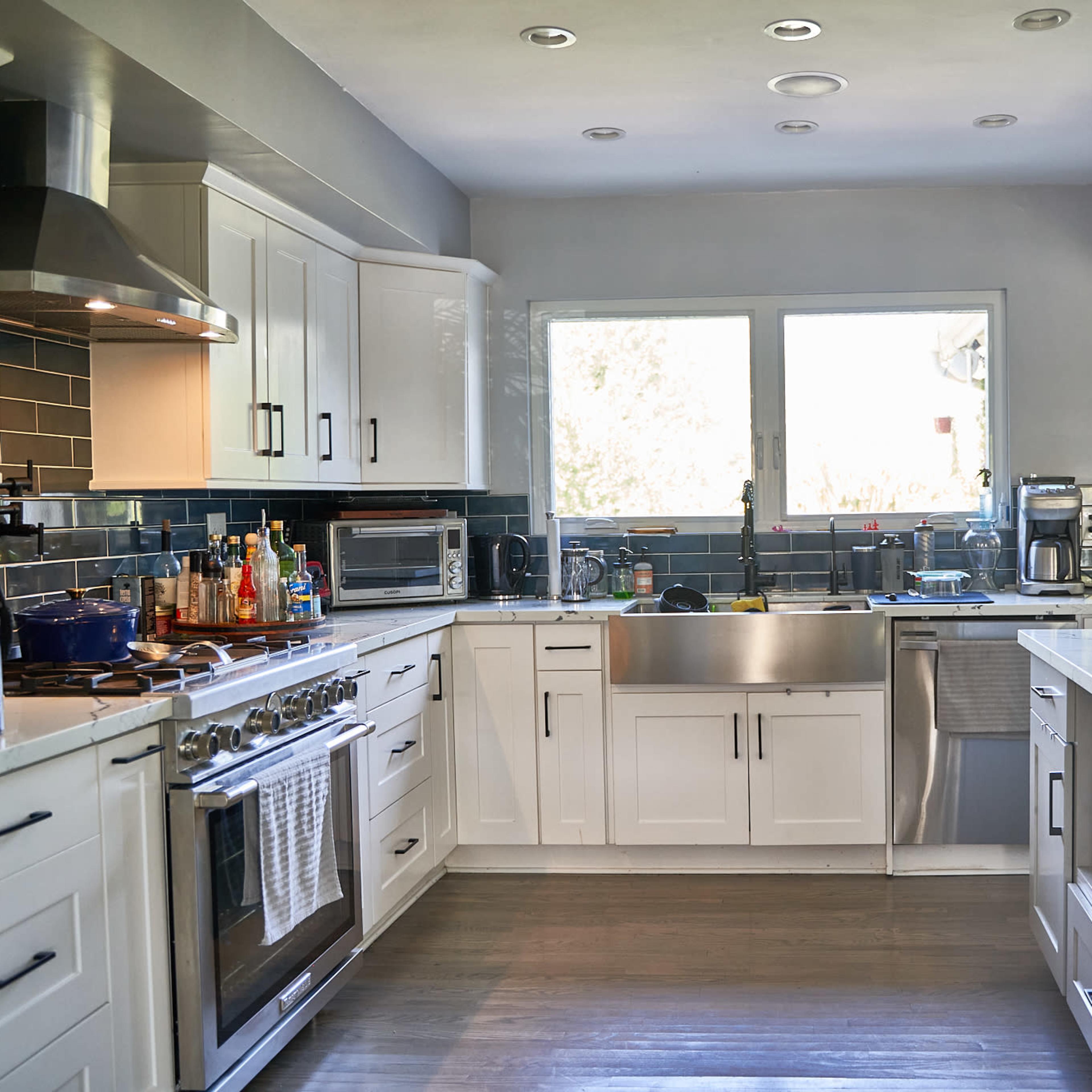 A modern kitchen equipped with stainless steel appliances, a large sink, and a marble countertop, illuminated by natural light from a window.