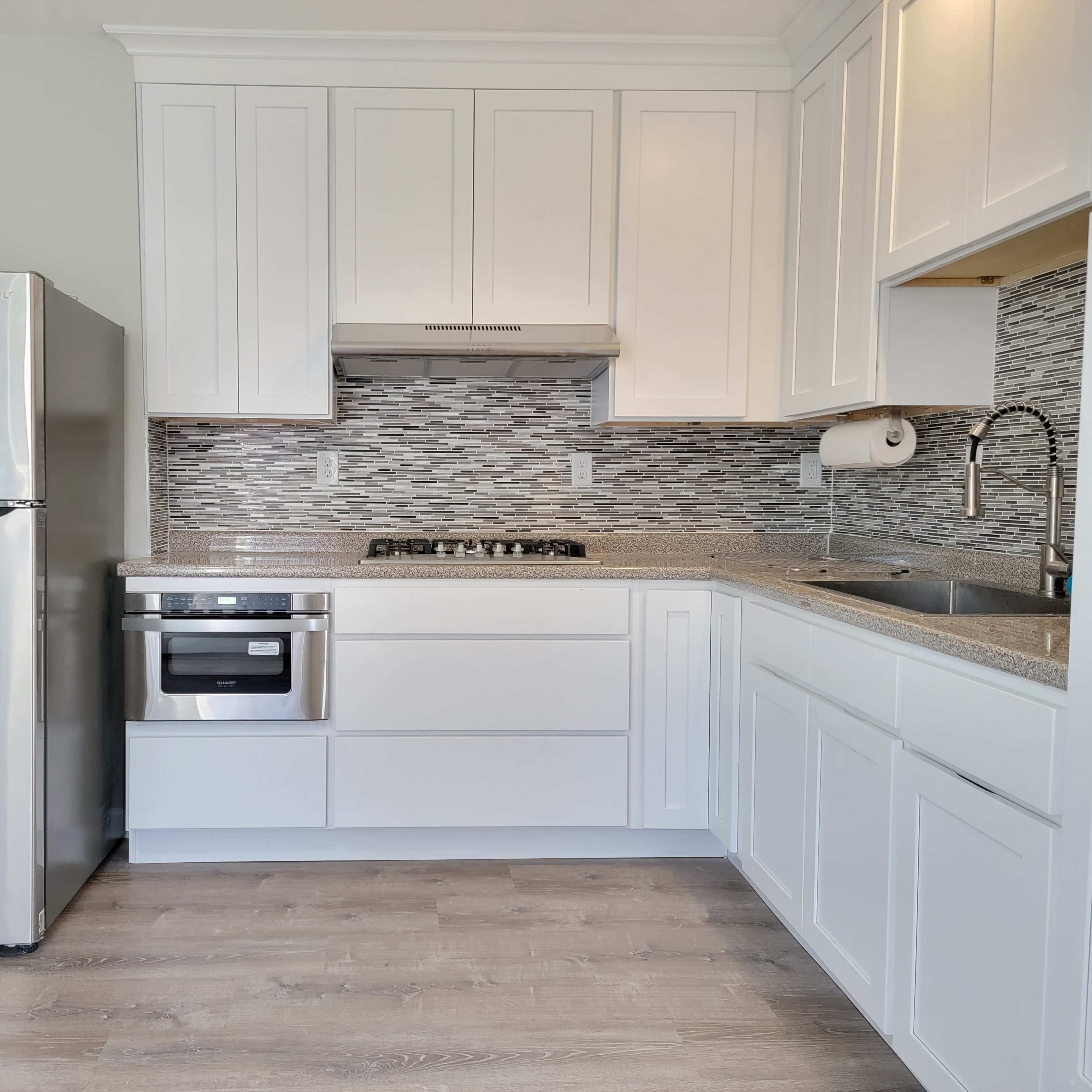 A modern kitchen featuring stainless steel appliances, white cabinetry, and a tiled backsplash.