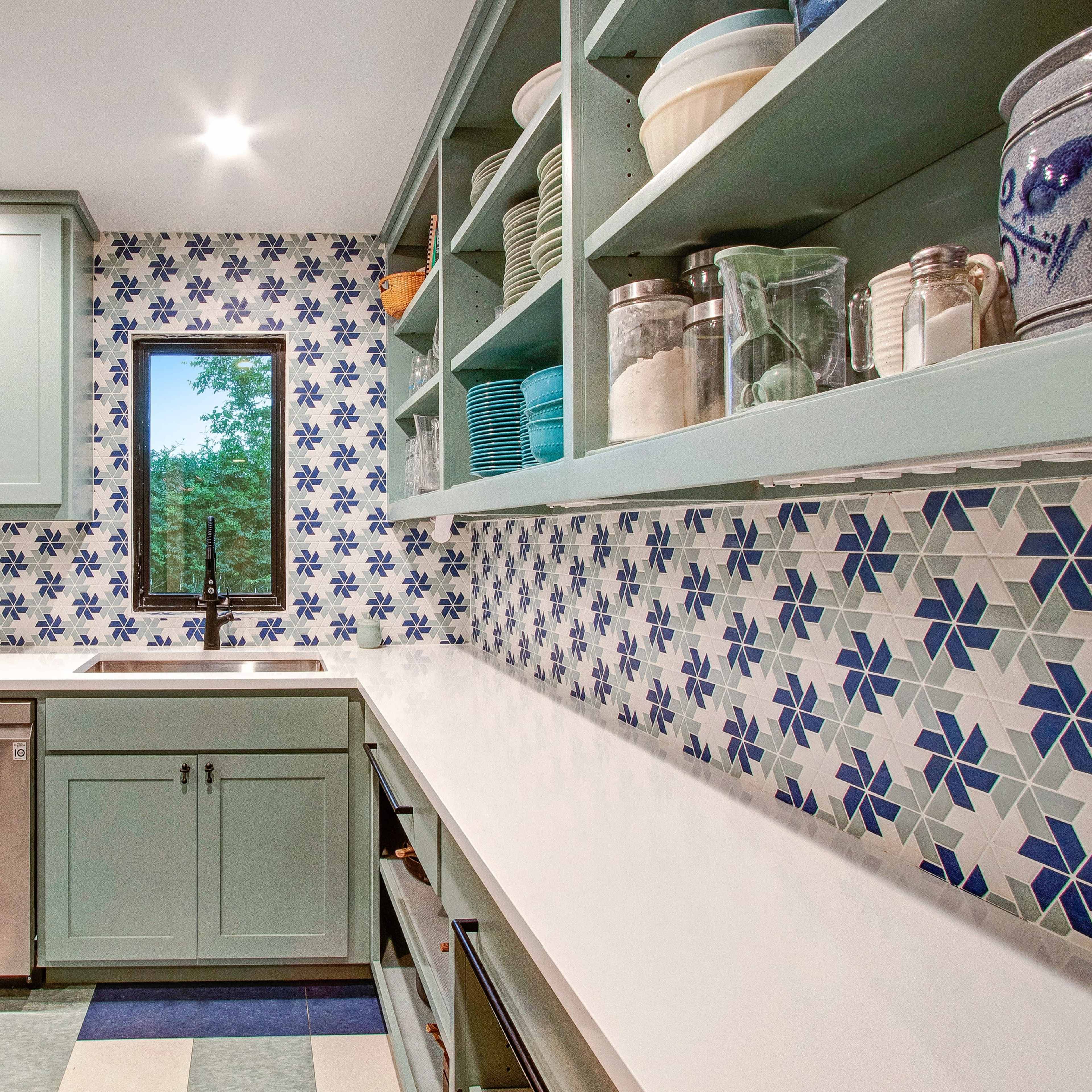 A modern kitchen features mint green cabinetry, a white countertop, and a patterned blue and white backsplash.