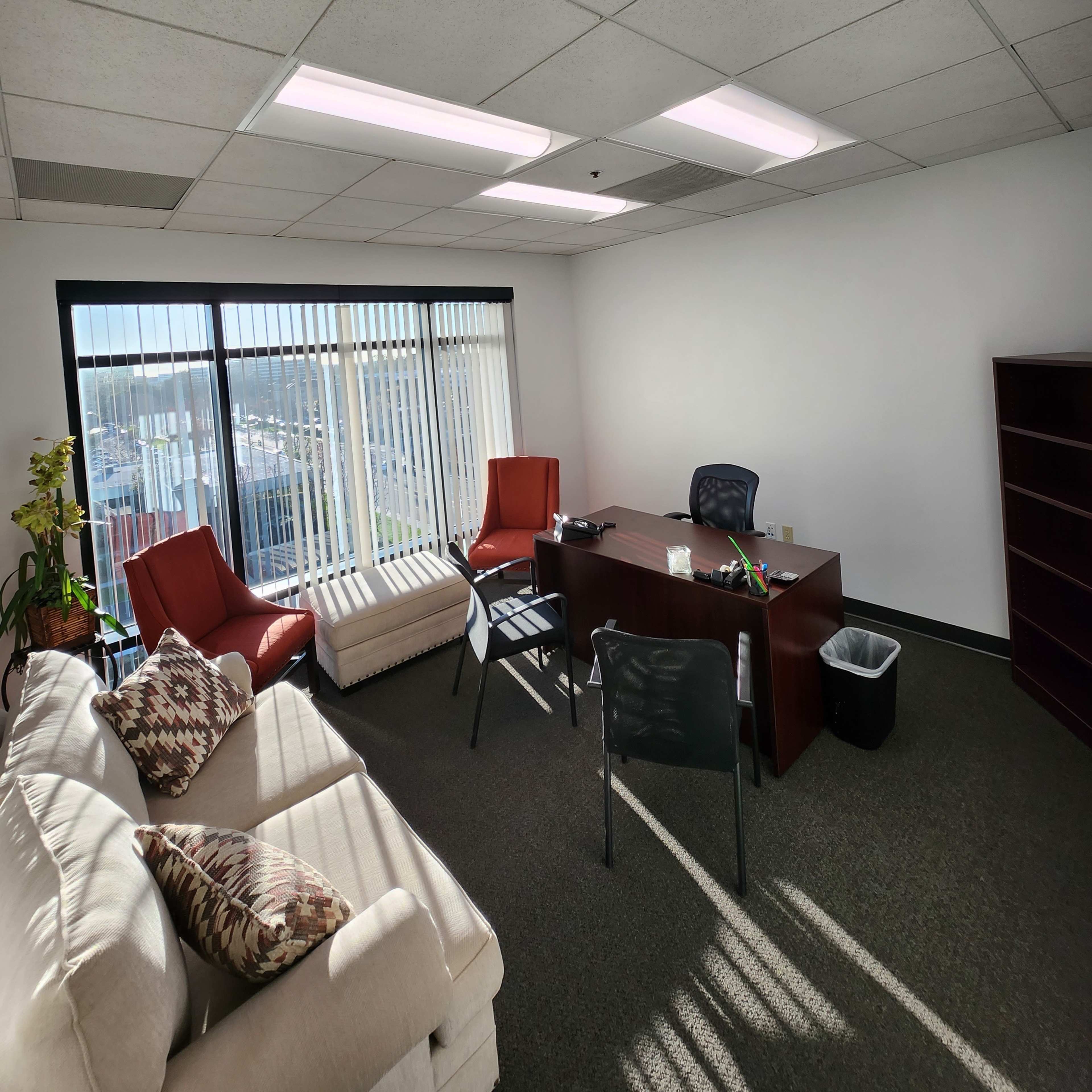 An office space with a desk, chairs, a couch, and large windows offering natural light.