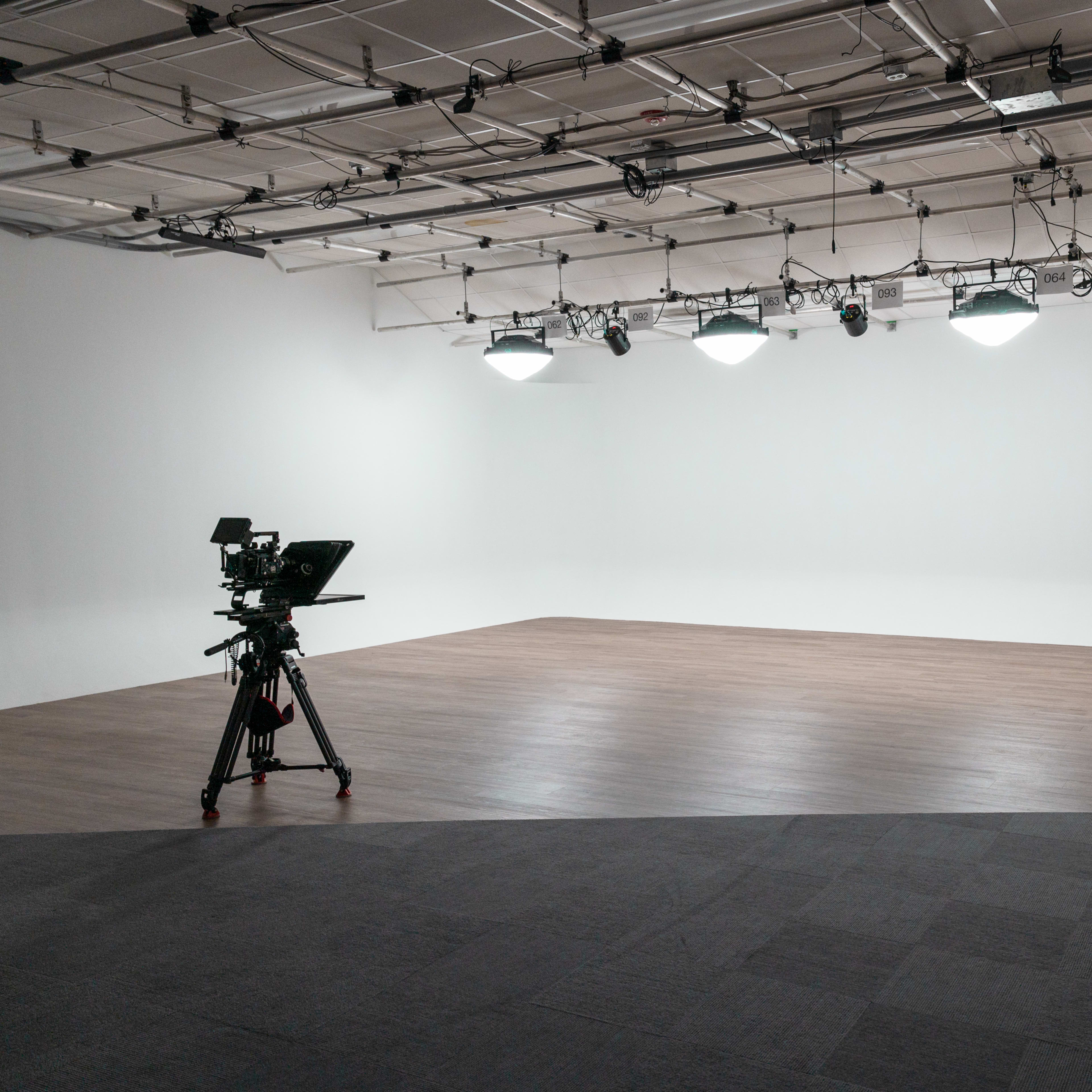 A minimalist studio space with a camera on a tripod, a ladder, and overhead lighting fixtures.