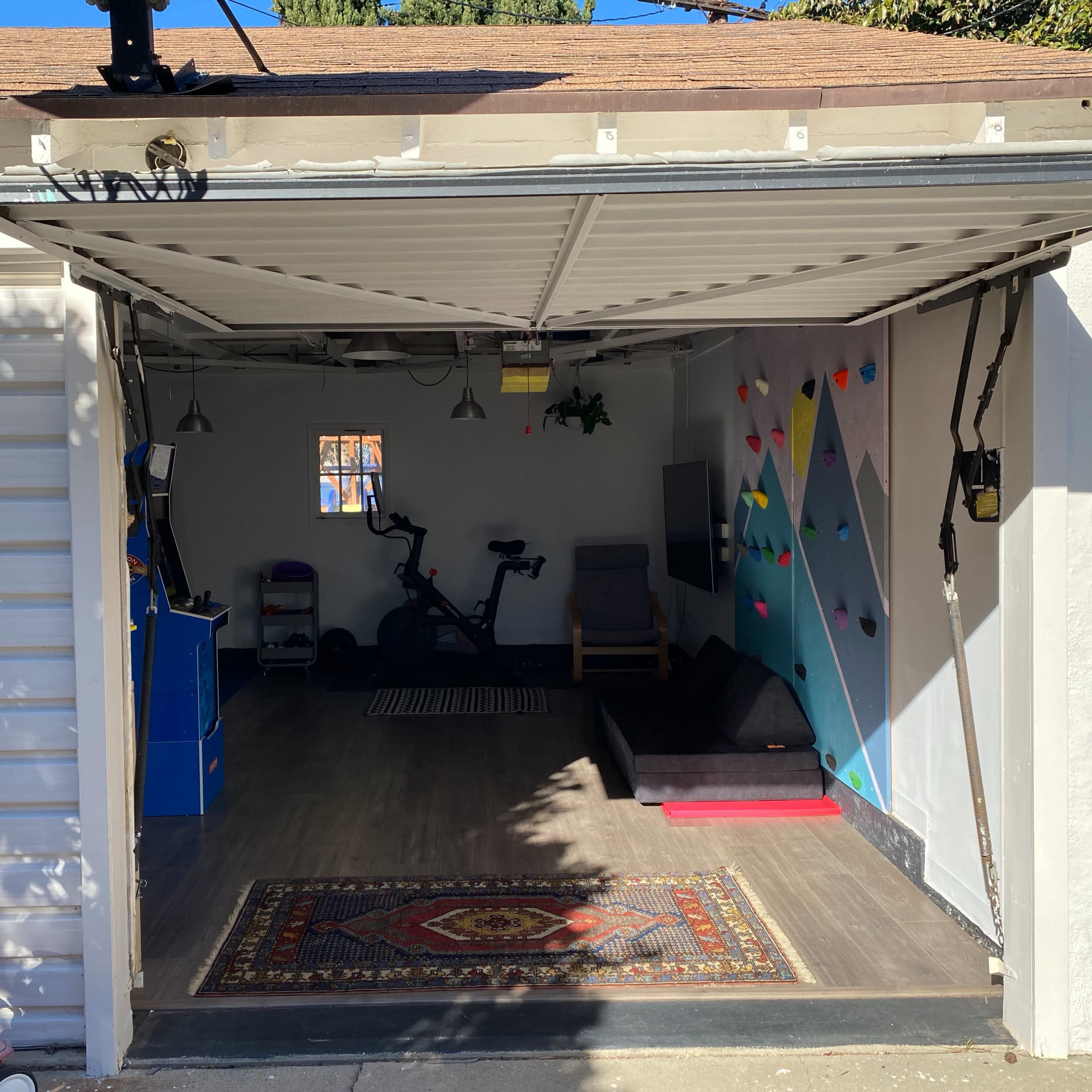 An open garage features a workout area with exercise equipment, a small bookshelf, and colorful wall decorations.