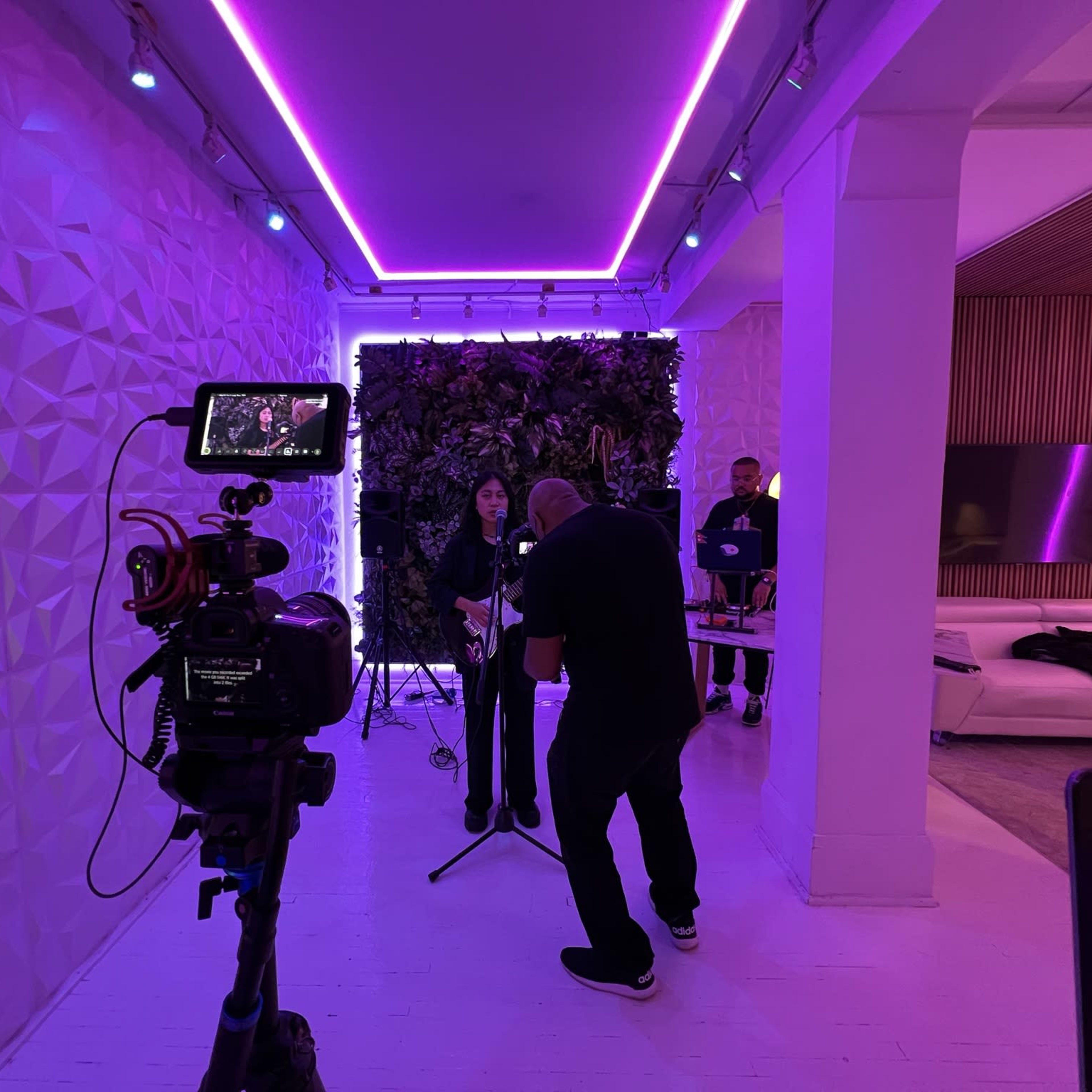 A singer performs in a modern studio with purple lighting while a videographer captures the scene.