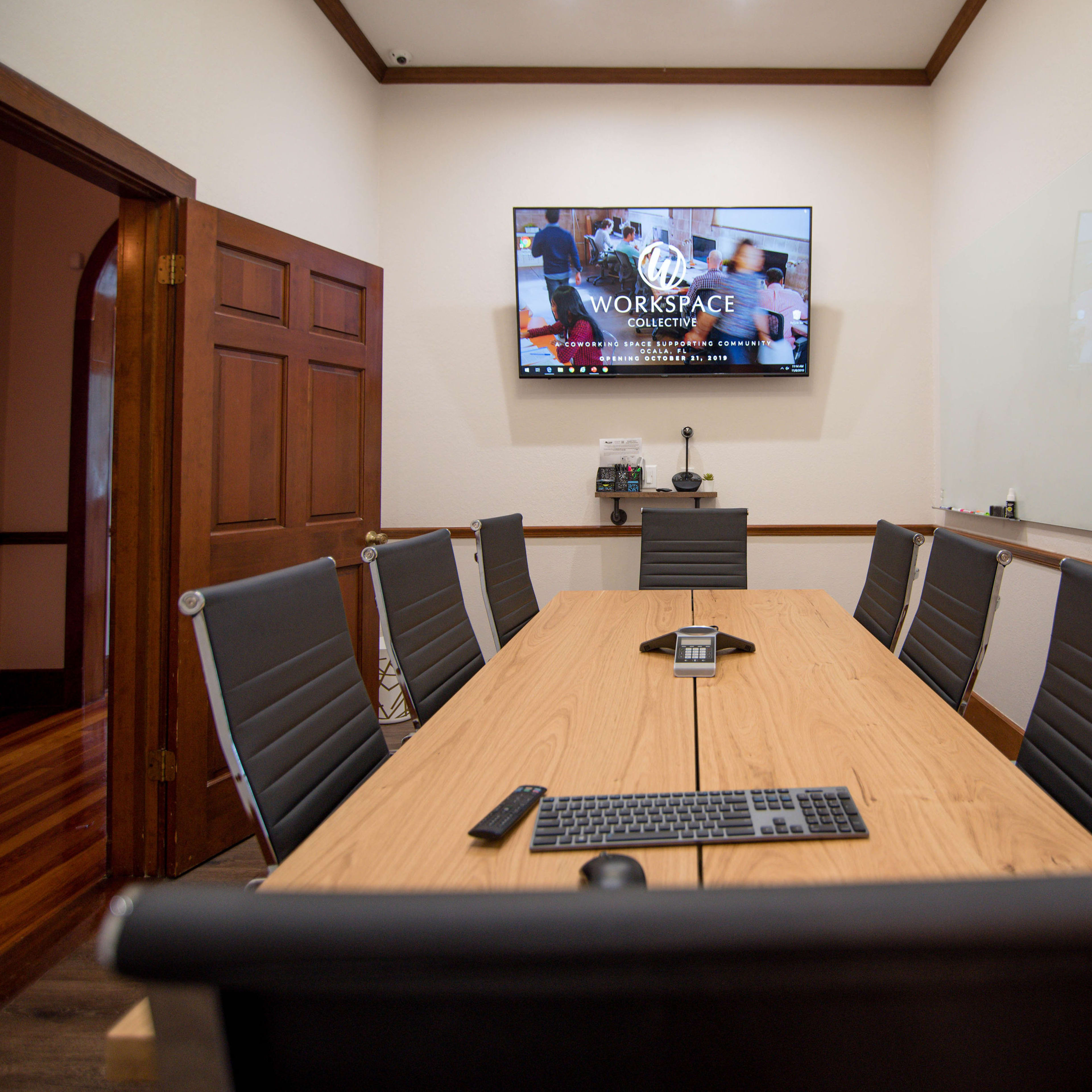A modern conference room with a large wooden table, black chairs, and a wall-mounted screen displaying the word "WORKSPACE."