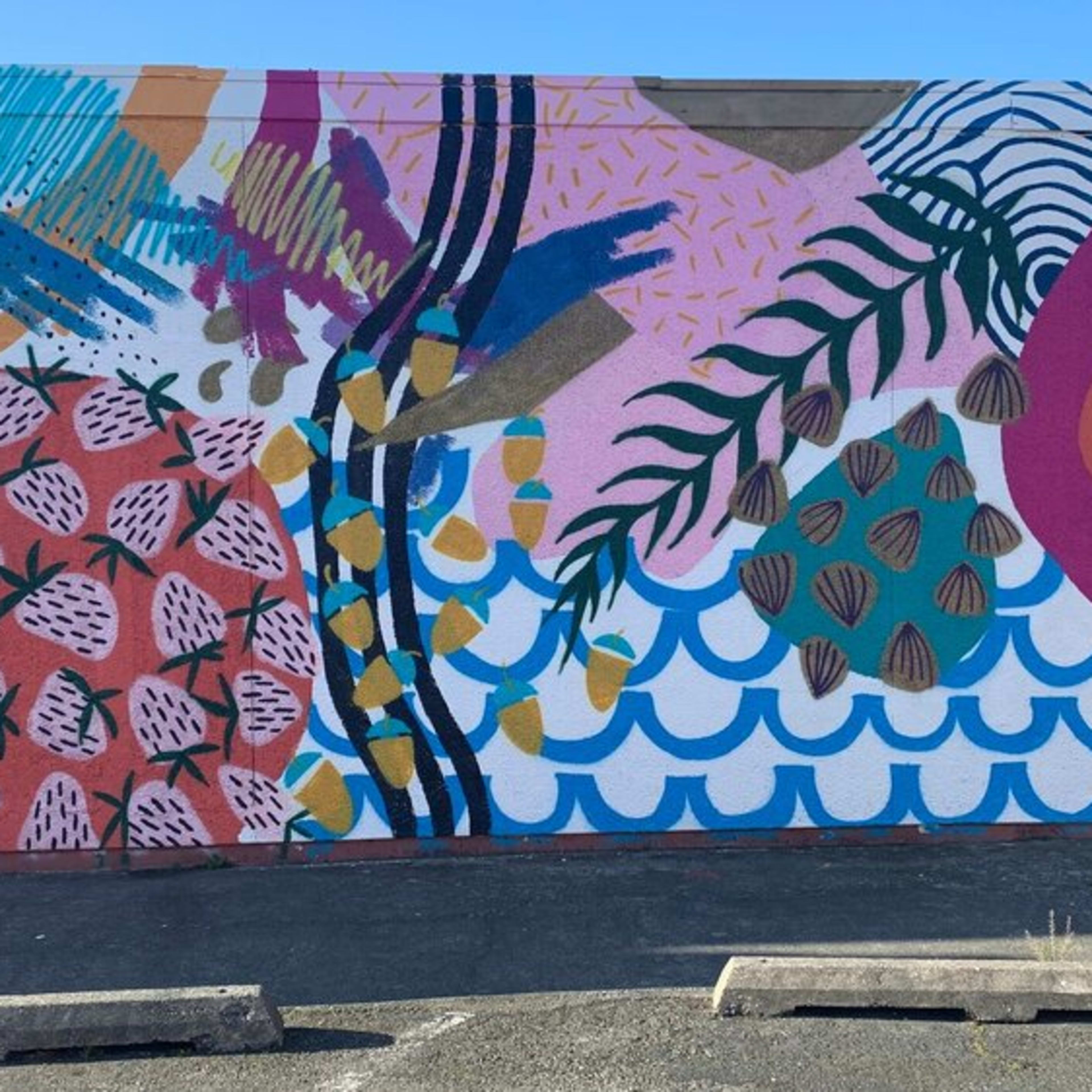 A colorful mural depicting various geometric shapes and tropical elements, including pineapples and waves, set against a pink background.